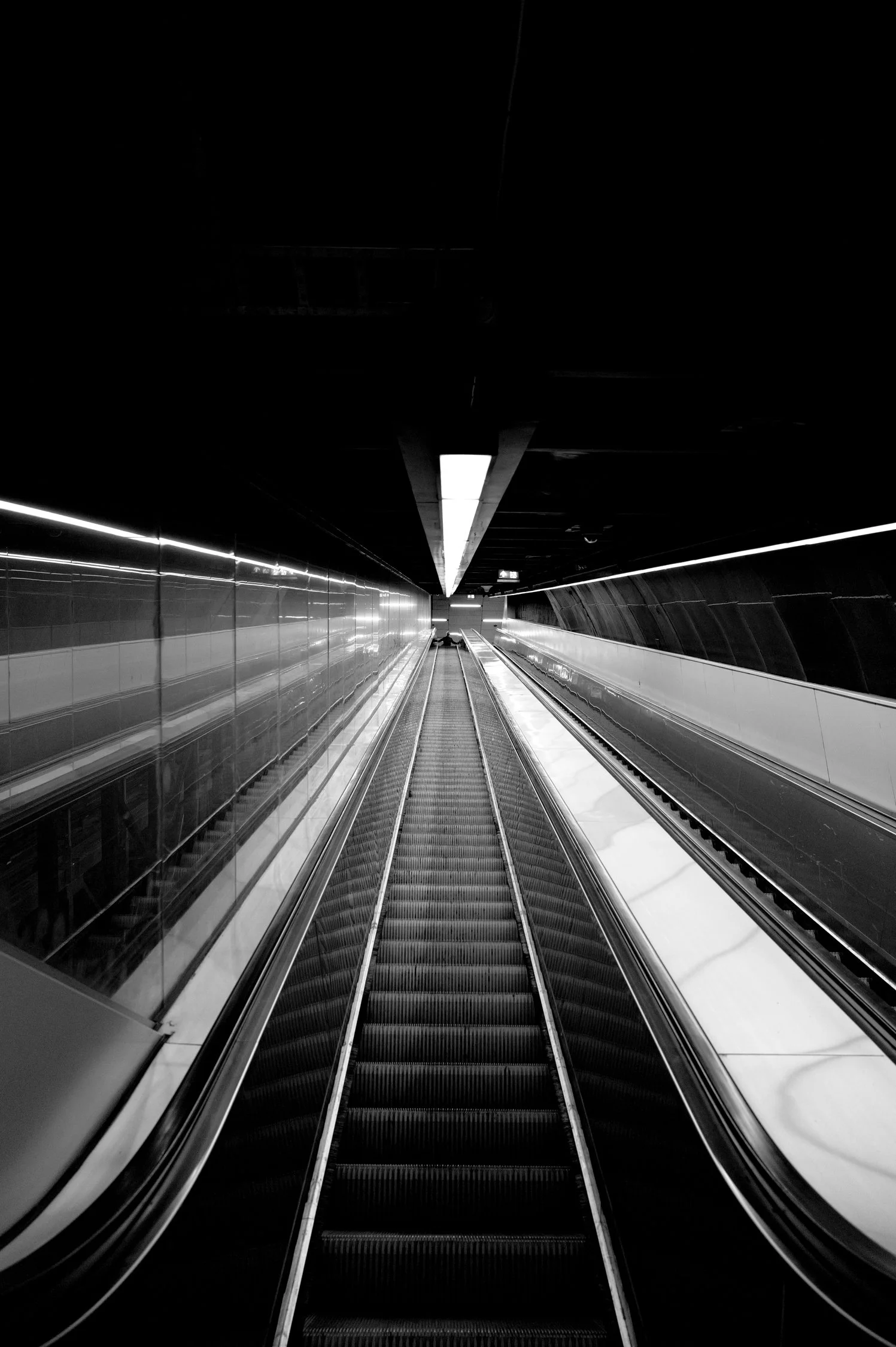 Un escalator dans une station de métro sombre, vue en perspective.