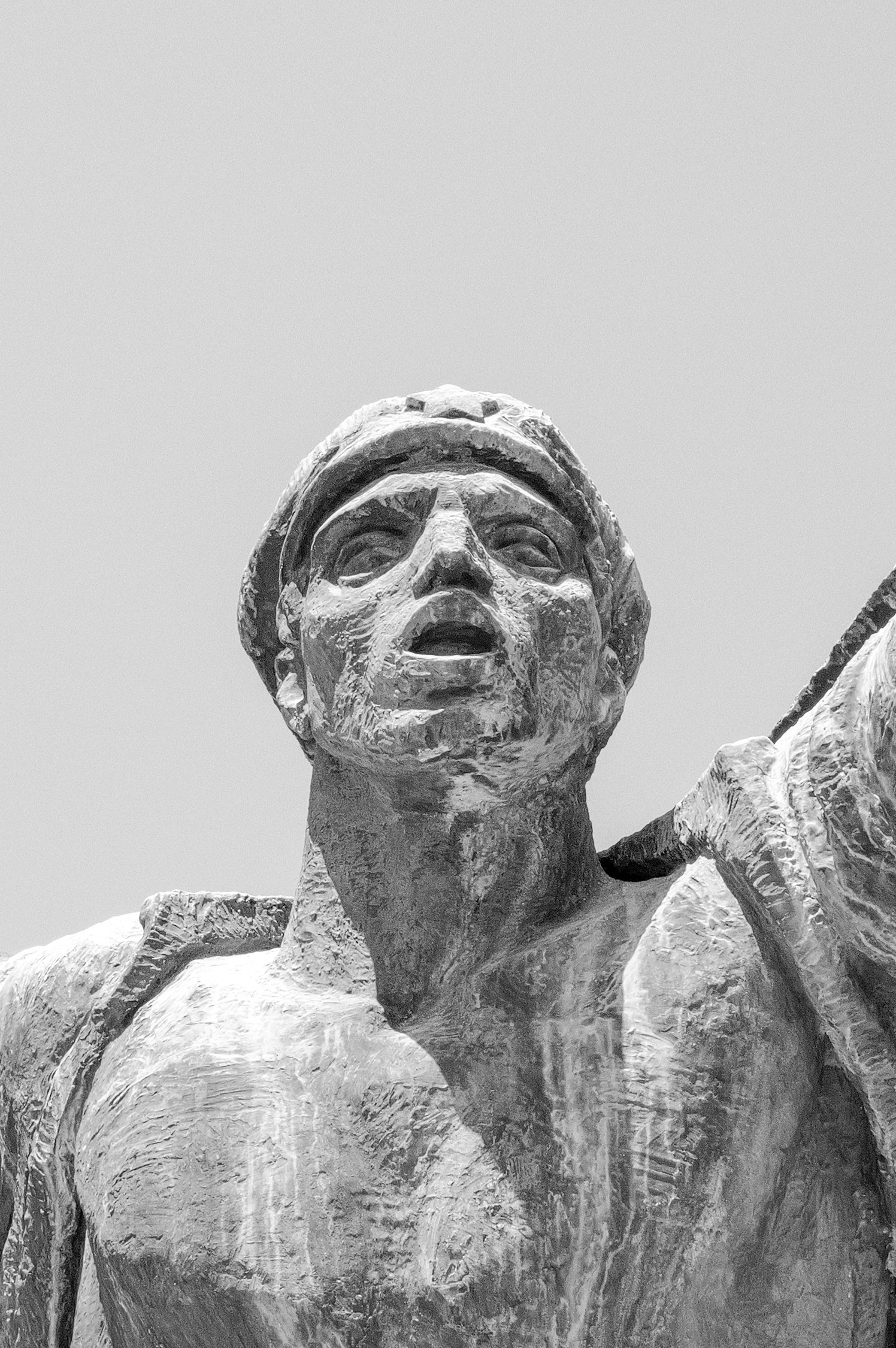 Une sculpture en pierre d'une figure humaine avec une tête couronnée, yeux fermés ou mi-clos, et une barbe épaisse, représentant probablement un personnage historique ou mythologique.