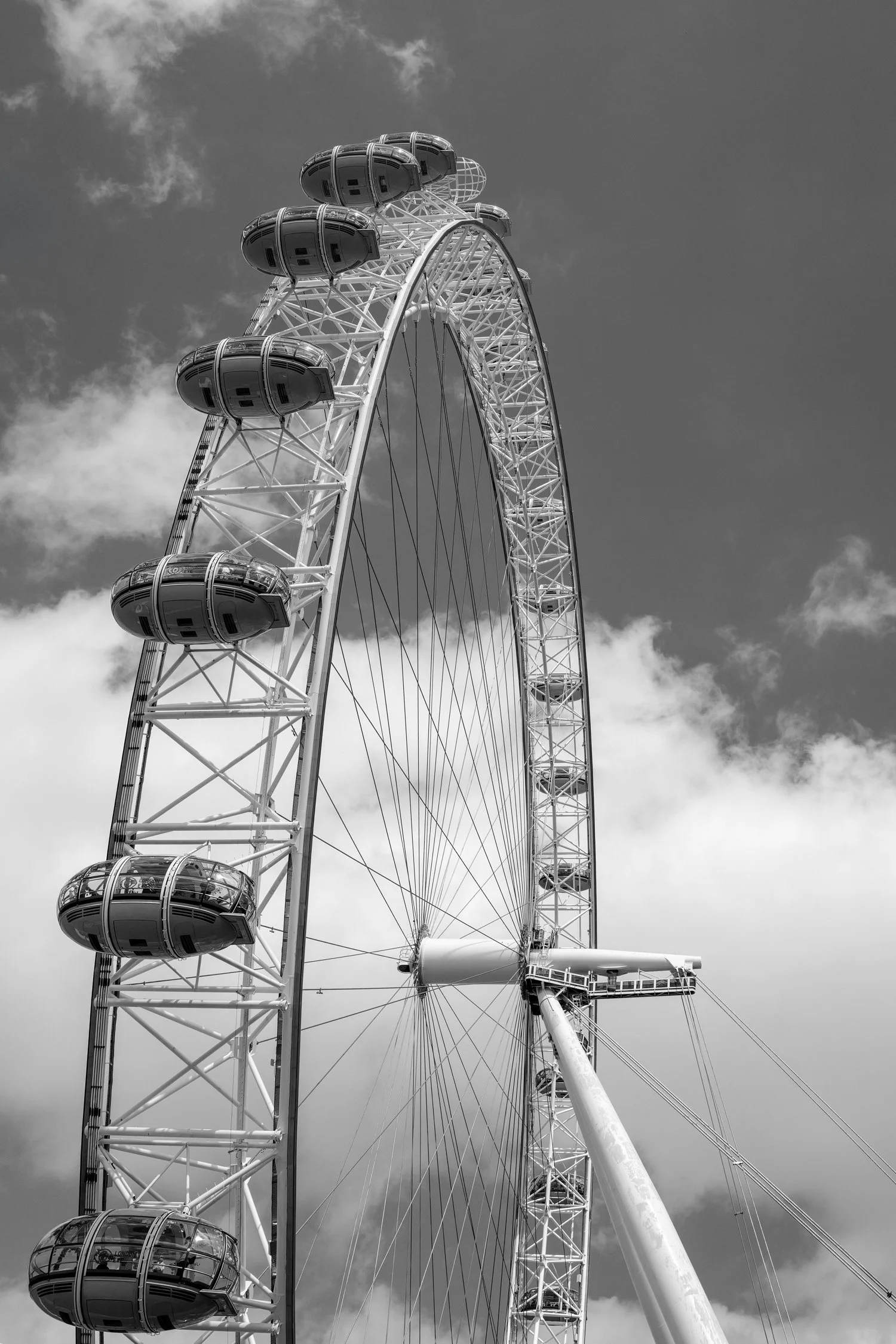 Une grande roue de foire avec des nacelles en forme de capsules, vue de dessous, sous un ciel nuageux.