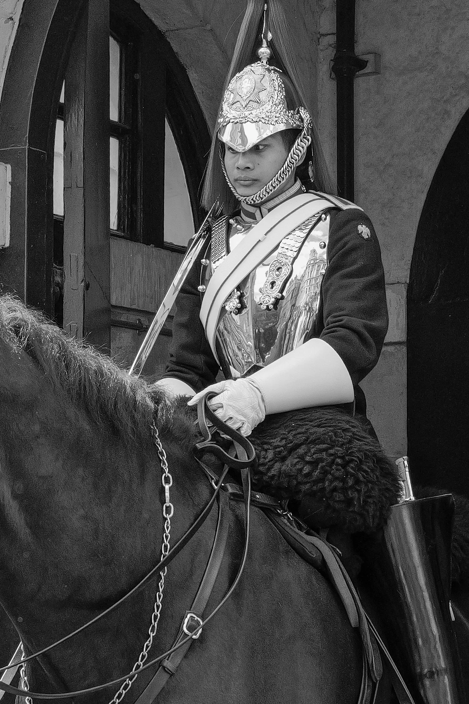 Une personne portant un uniforme de garde royale ou maréchal à cheval, avec un casque décoré, en train de monter un cheval noir.