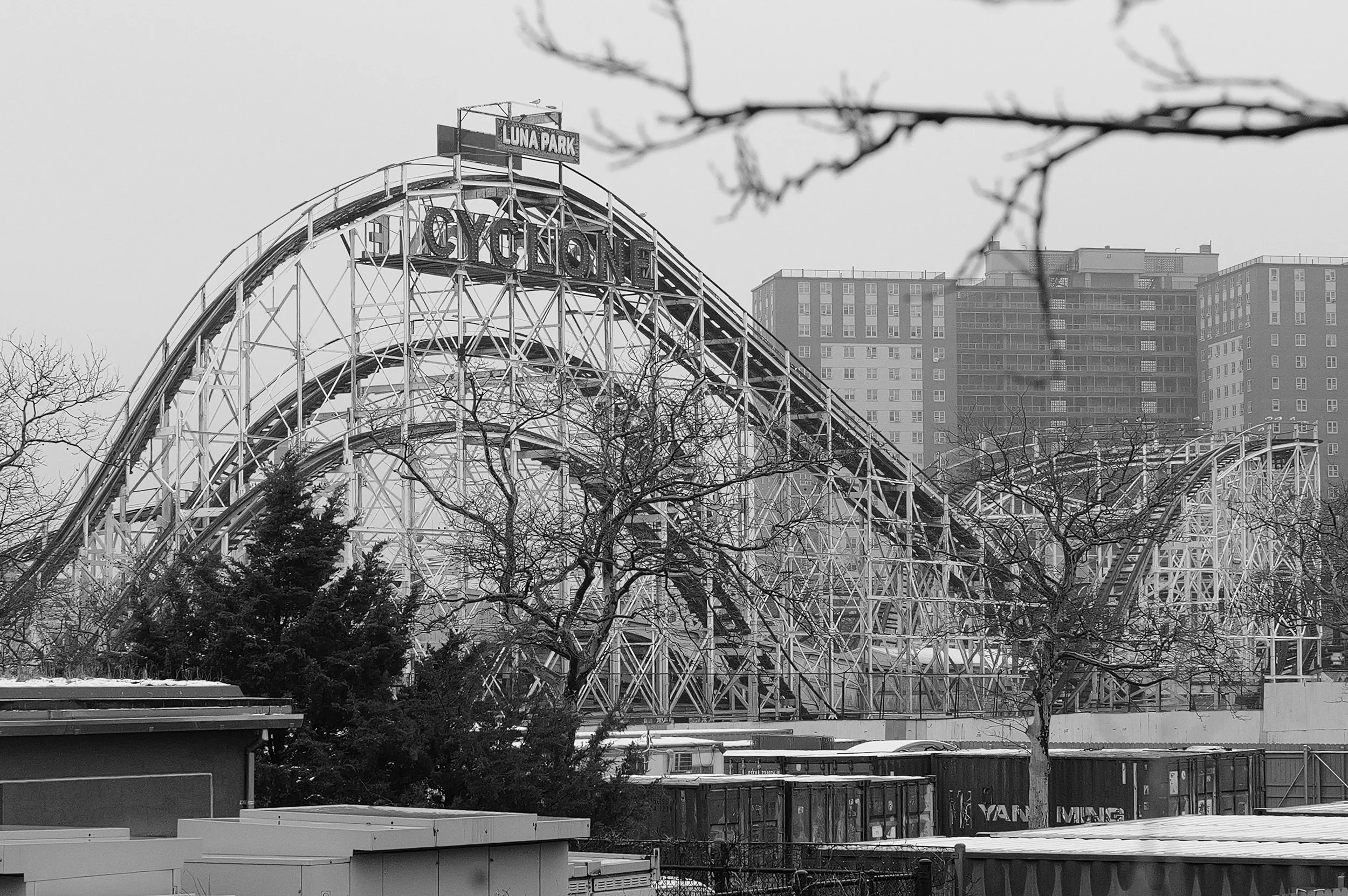 Montagnes russes en acier à Luna Park, avec des bâtiments résidentiels en arrière-plan, en noir et blanc.