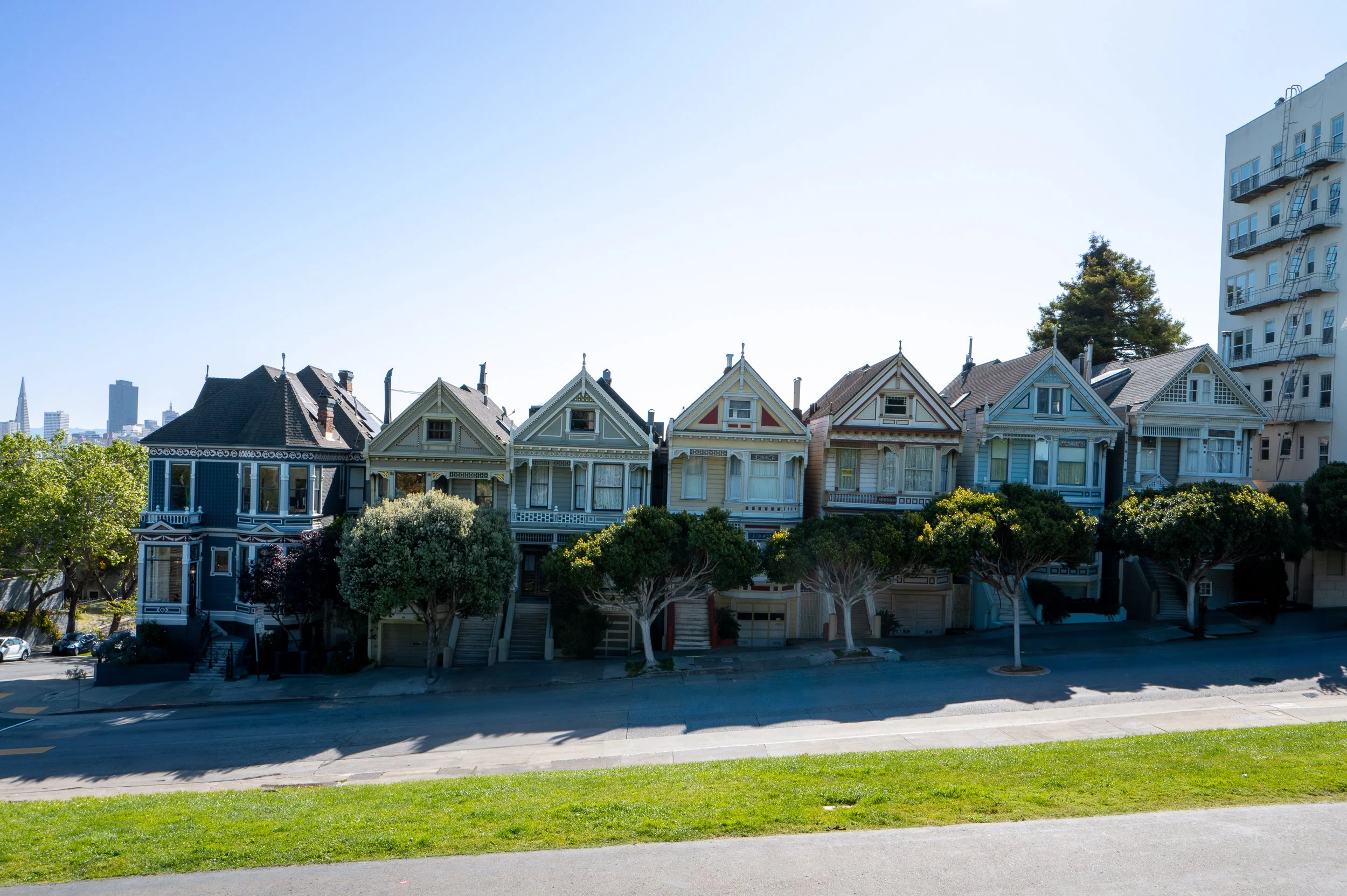 Une rangée de maisons victoriennes colorées avec des arbres en premier plan, dans une zone urbaine