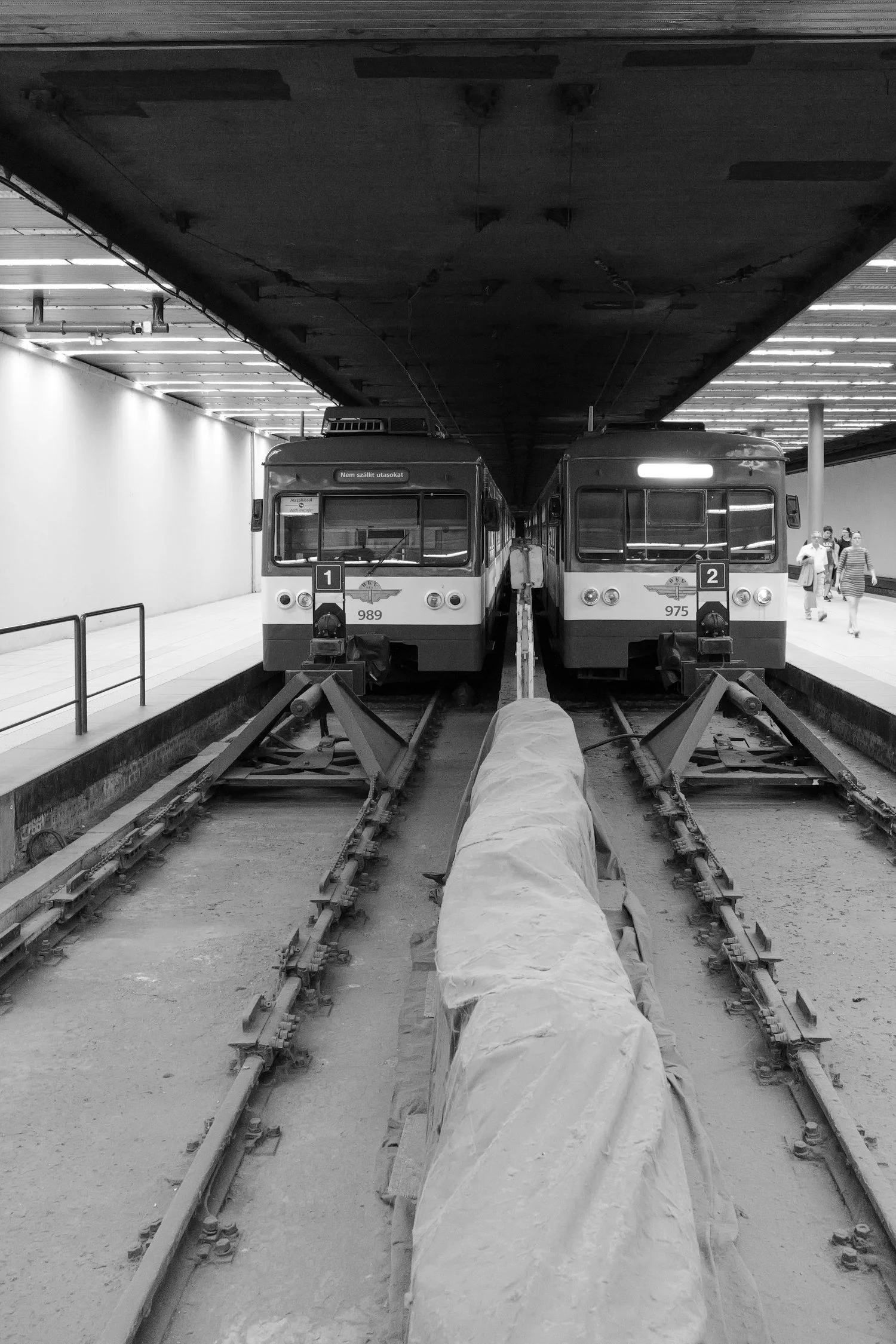 Deux trains dans une station souterraine, en cours de construction ou de rénovation, avec des ouvriers et des équipements de chantier autour.