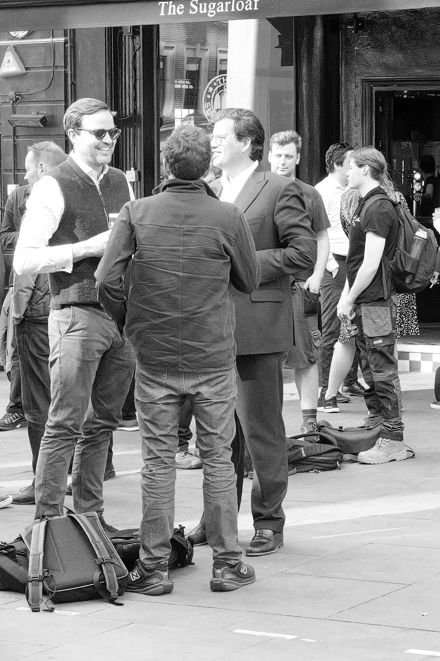 Groupe de jeunes adultes discutant dans la rue, certains portant des sacs à dos et des appareils photo.