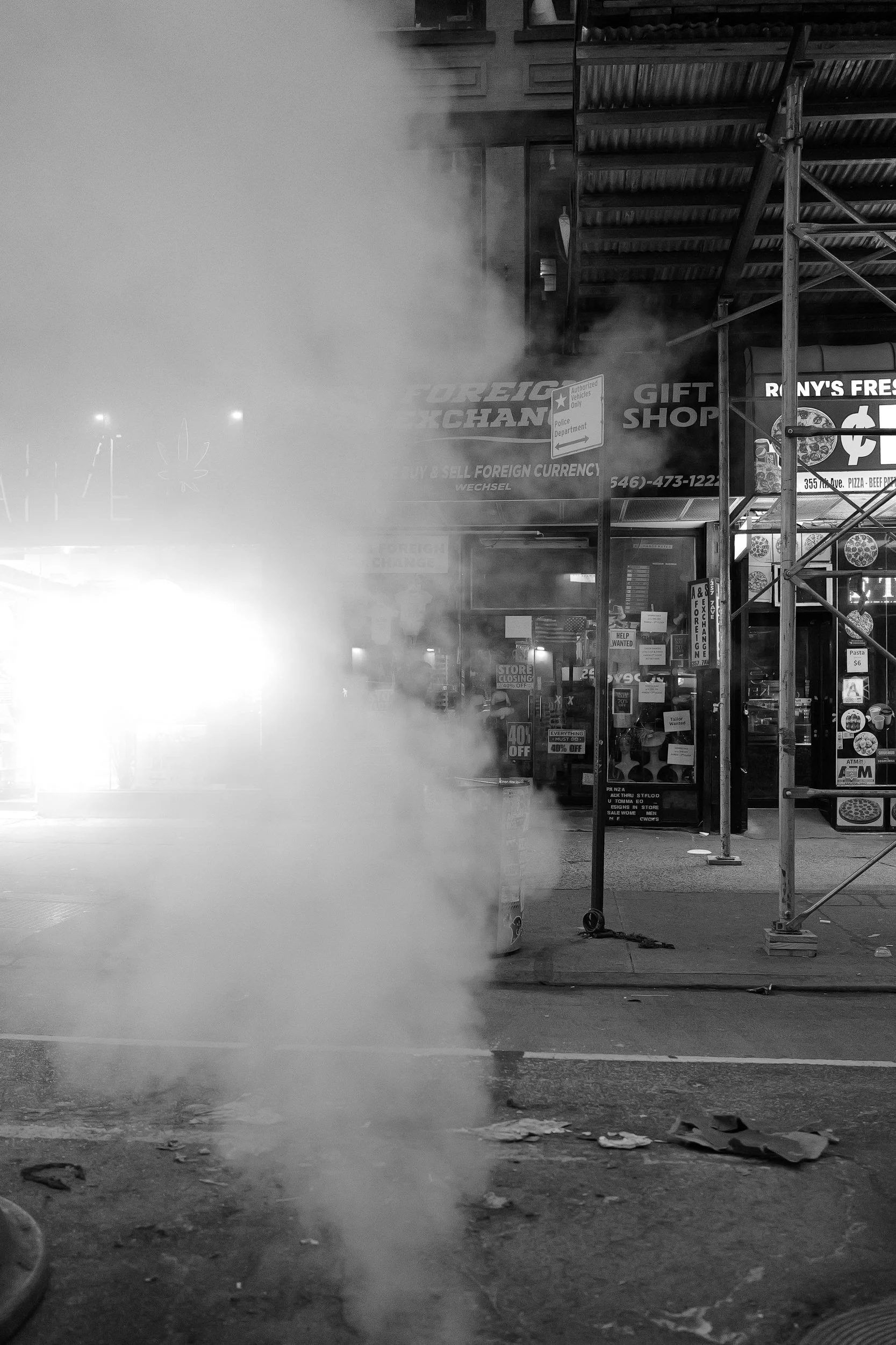 Une scène de rue avec de la fumée ou de la vapeur devant un magasin d'échange de devises étrangères, des panneaux publicitaires et une structure en scaffolding.