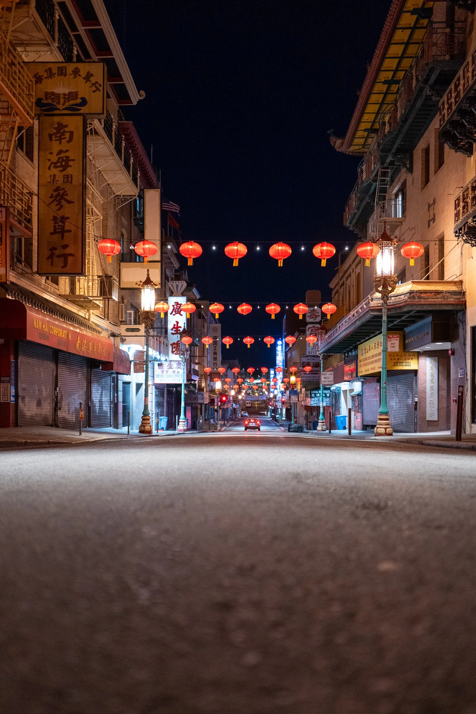 Rue vide dans un quartier asiatique, décorée de lanternes rouges suspendues, avec des bâtiments traditionnels et des lampadaires le long du trottoir, la nuit.