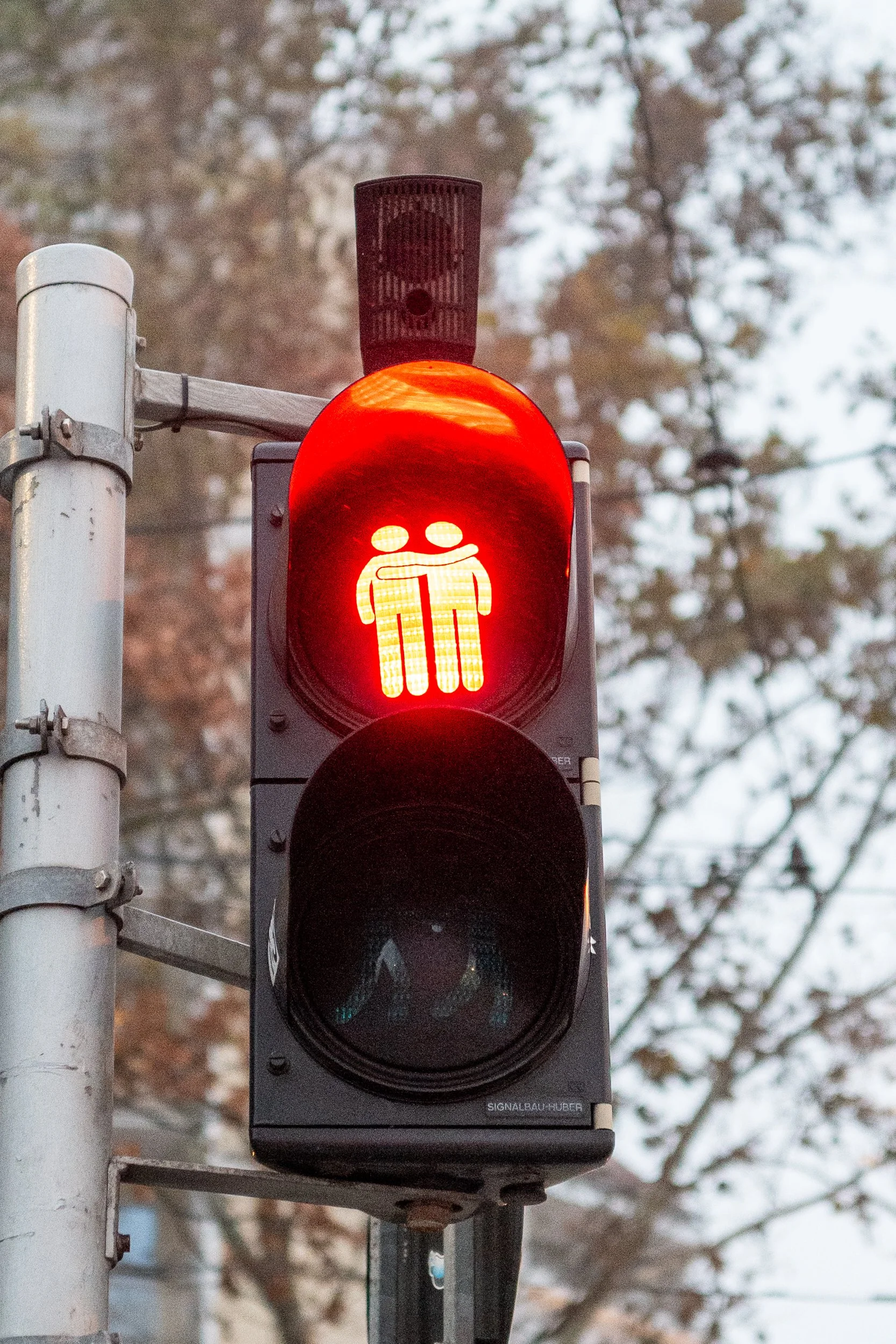 Feu rouge piétons avec symbole de deux personnes, une d'entre elles semble embrasser l'autre.