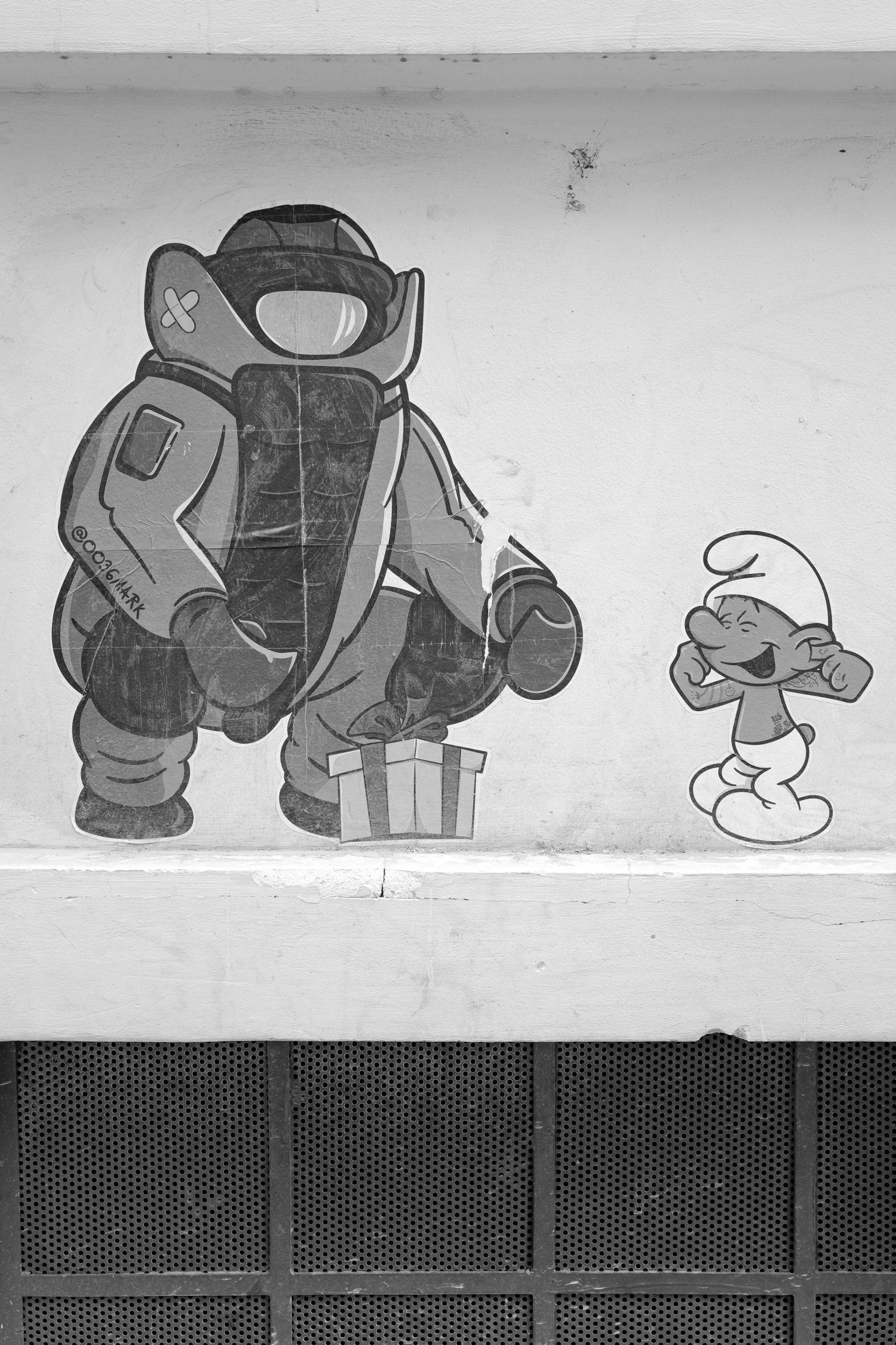 Une peinture murale en noir et blanc représentant un personnage de bande dessinée souriant avec les yeux fermés et la main levée, à côté d’un autre personnage qui est un peu moins visible.