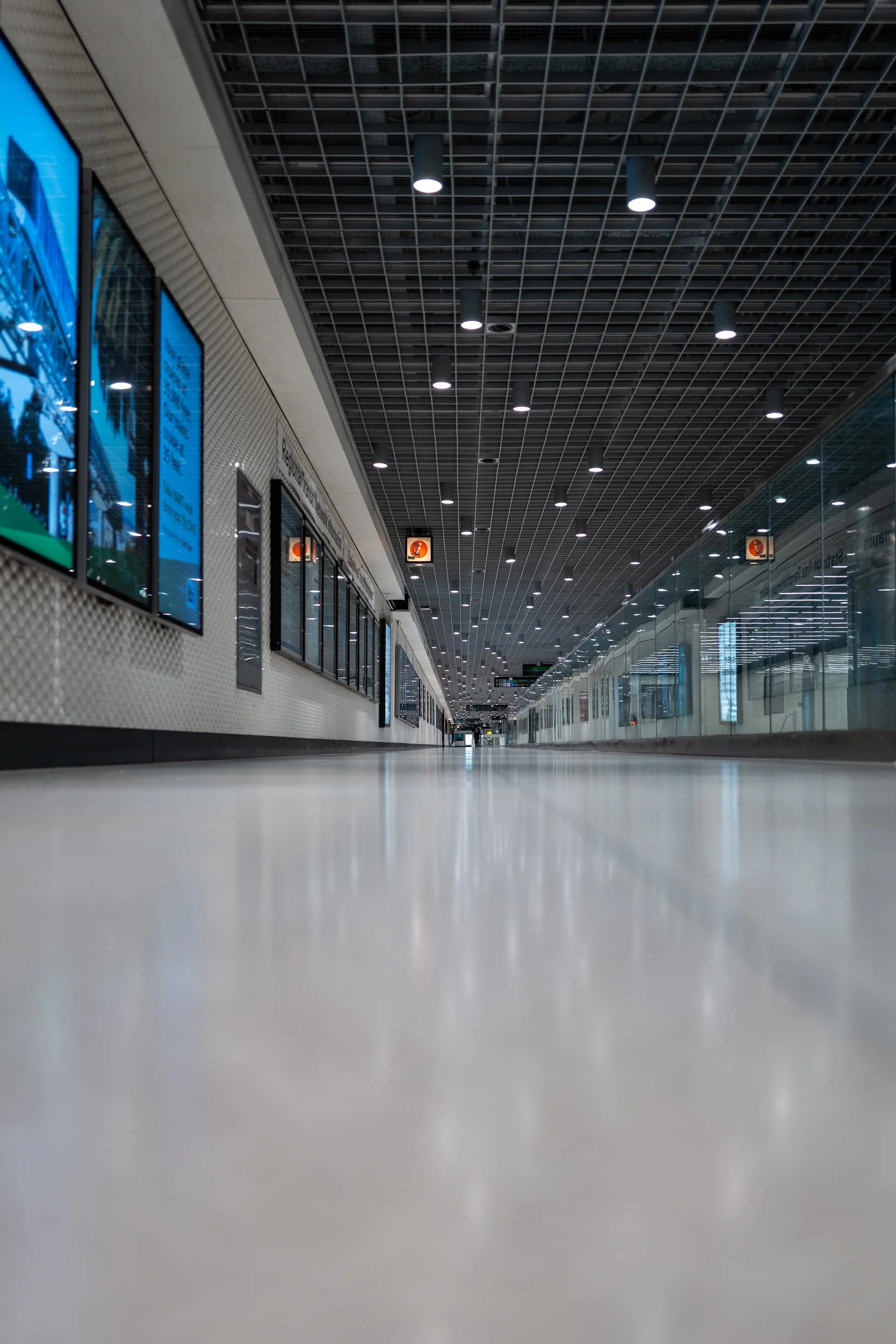 Un couloir d'aéroport ou de métro vide vu du sol avec des écrans d'informations et un plafond noir avec des lumières.