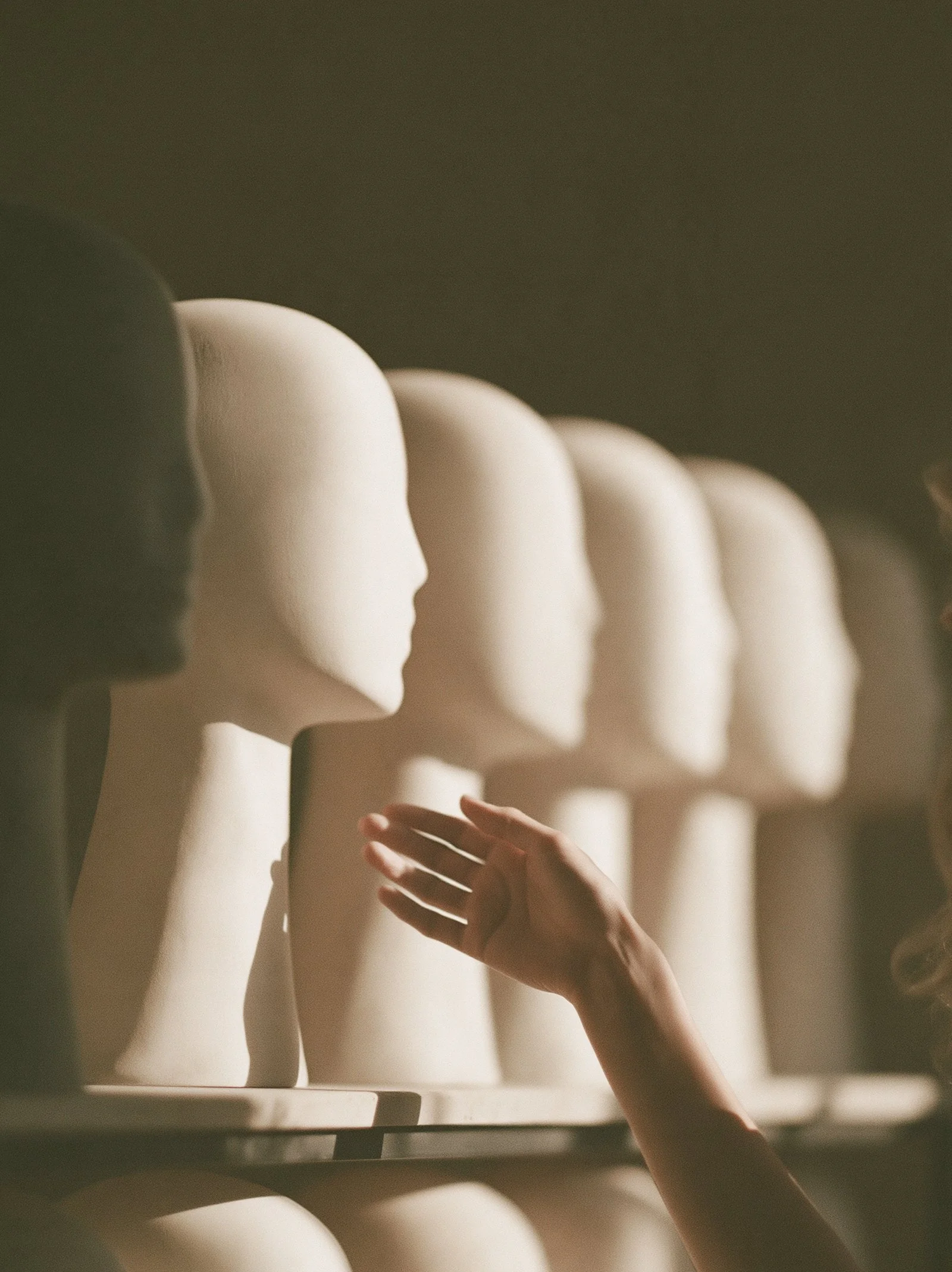 A row of blank mannequin heads in a salon with one real hand resting on the middle head.