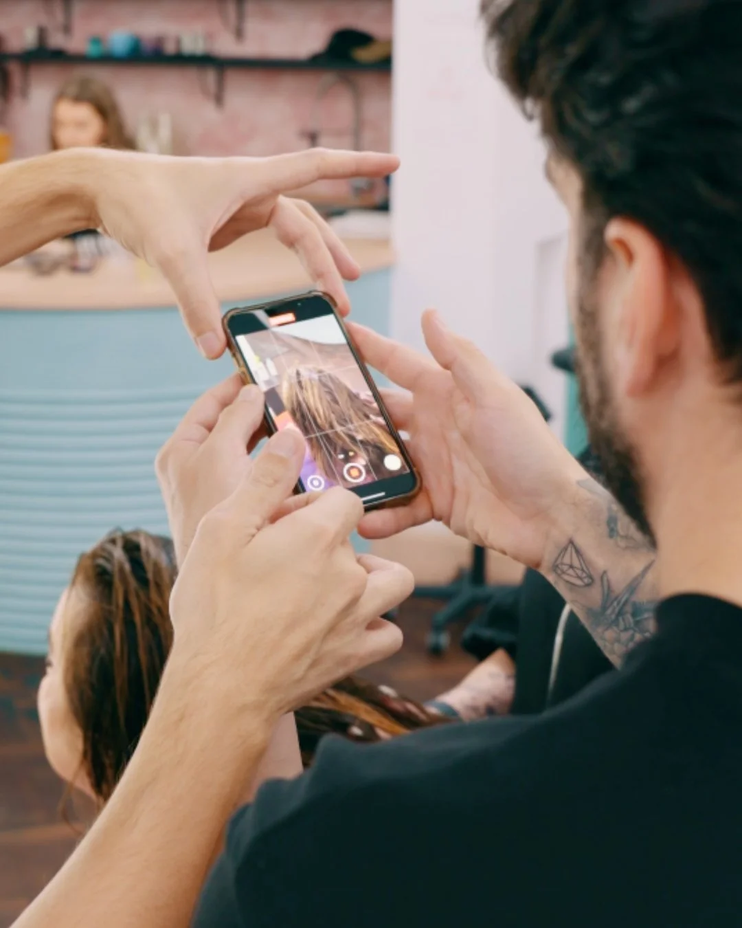 A person taking a photo with a smartphone of another person with dreadlocks, in a salon or studio setting.