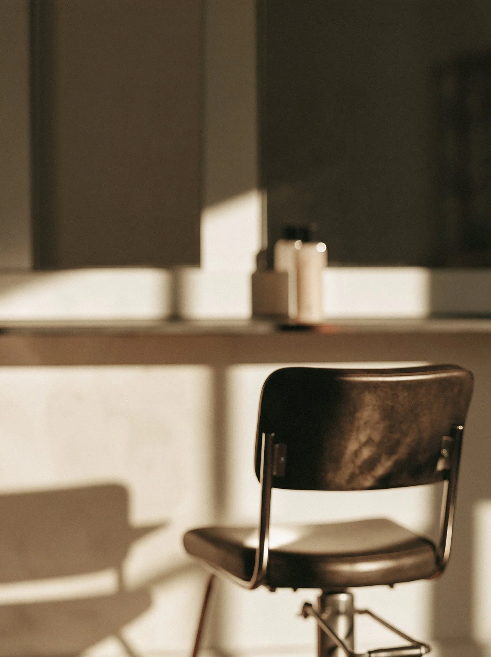 An empty salon chair facing a mirror with a single product bottle beside it.