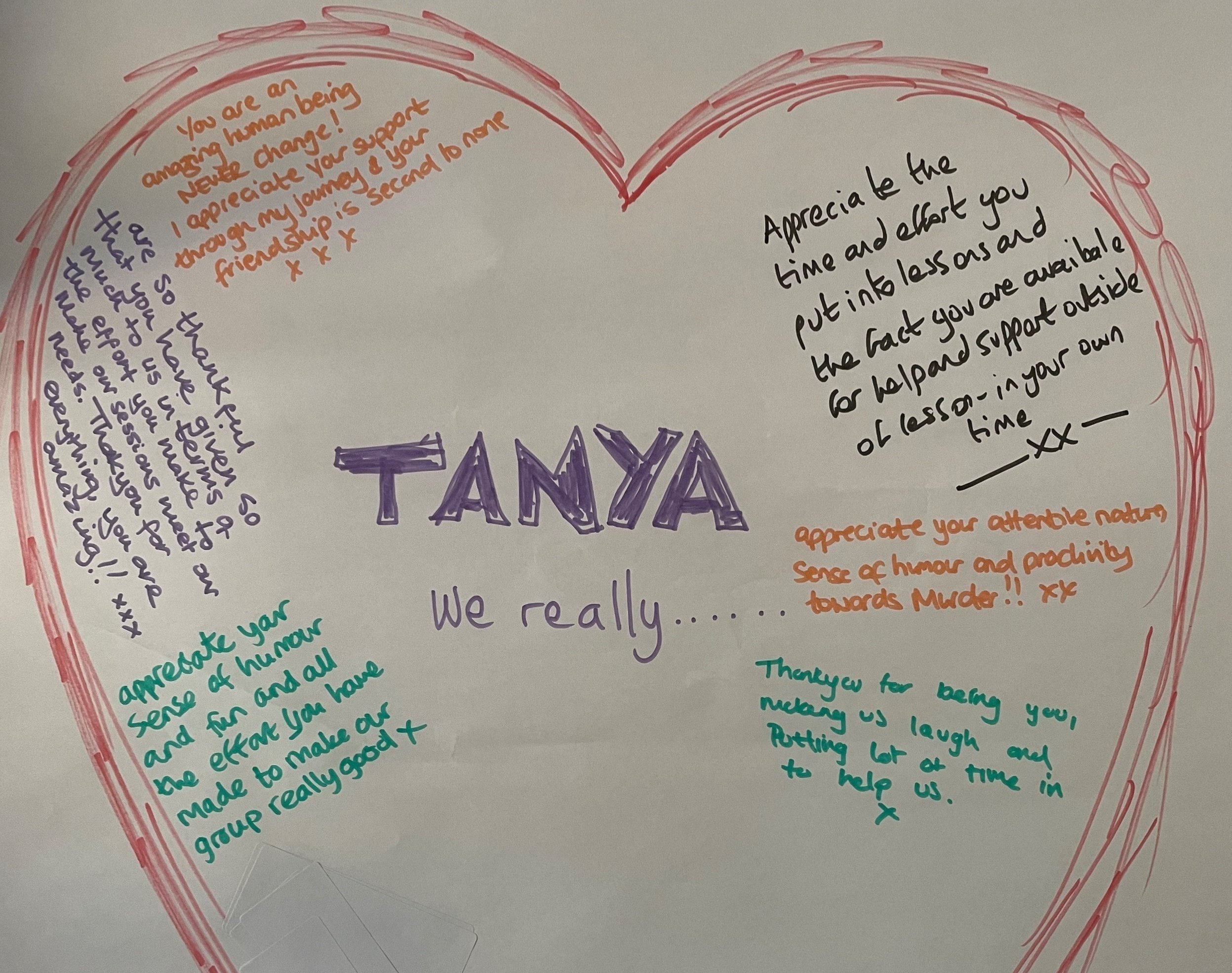 A heart-shaped card with colorful handwritten messages from multiple people. The center features the name 'TANYA' in large purple letters, with the words 'We really...' written below. Each side of the heart contains personal notes praising Tanya's hu