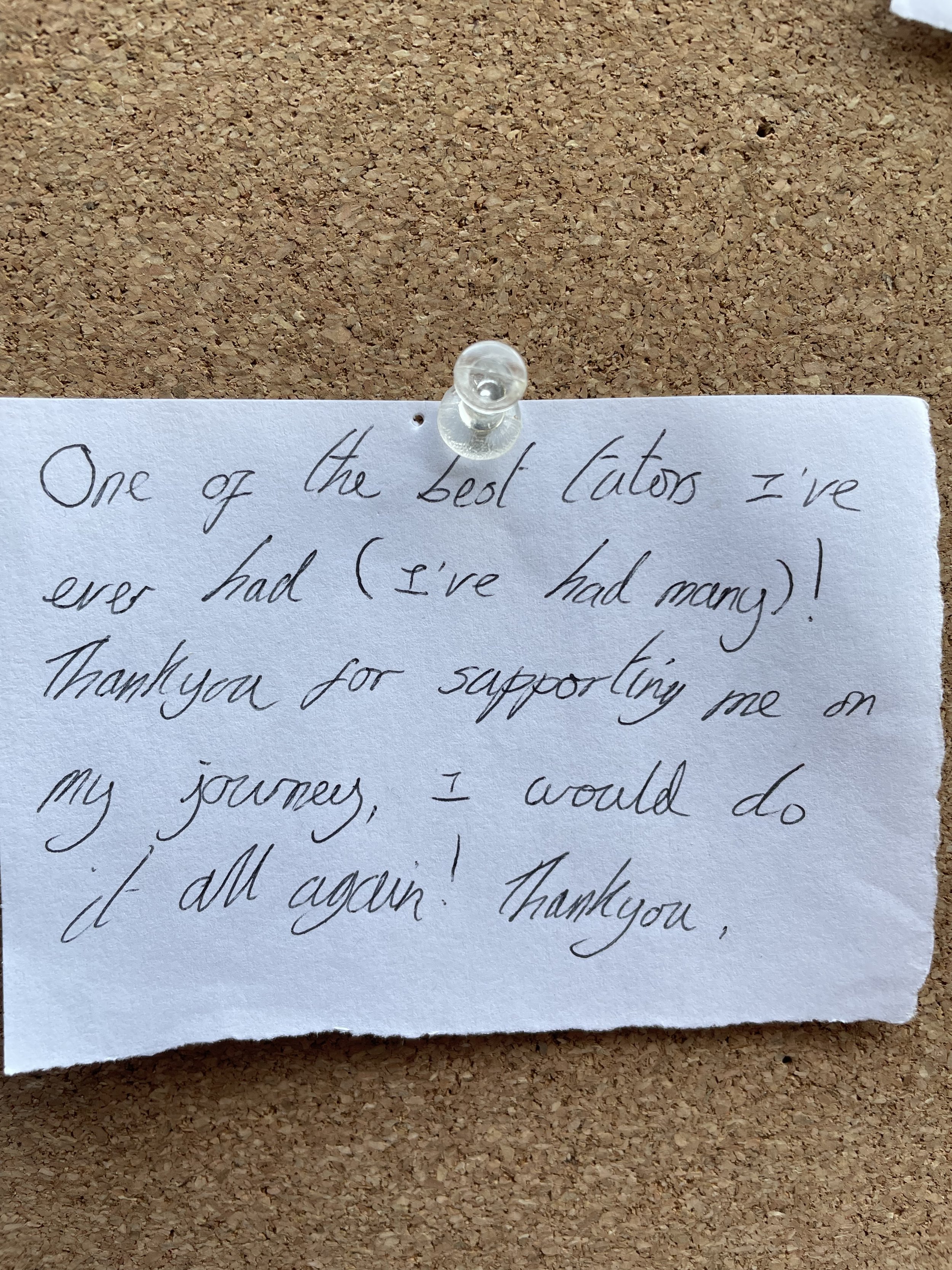 A handwritten thank you note pinned to a corkboard with a clear thumbtack.