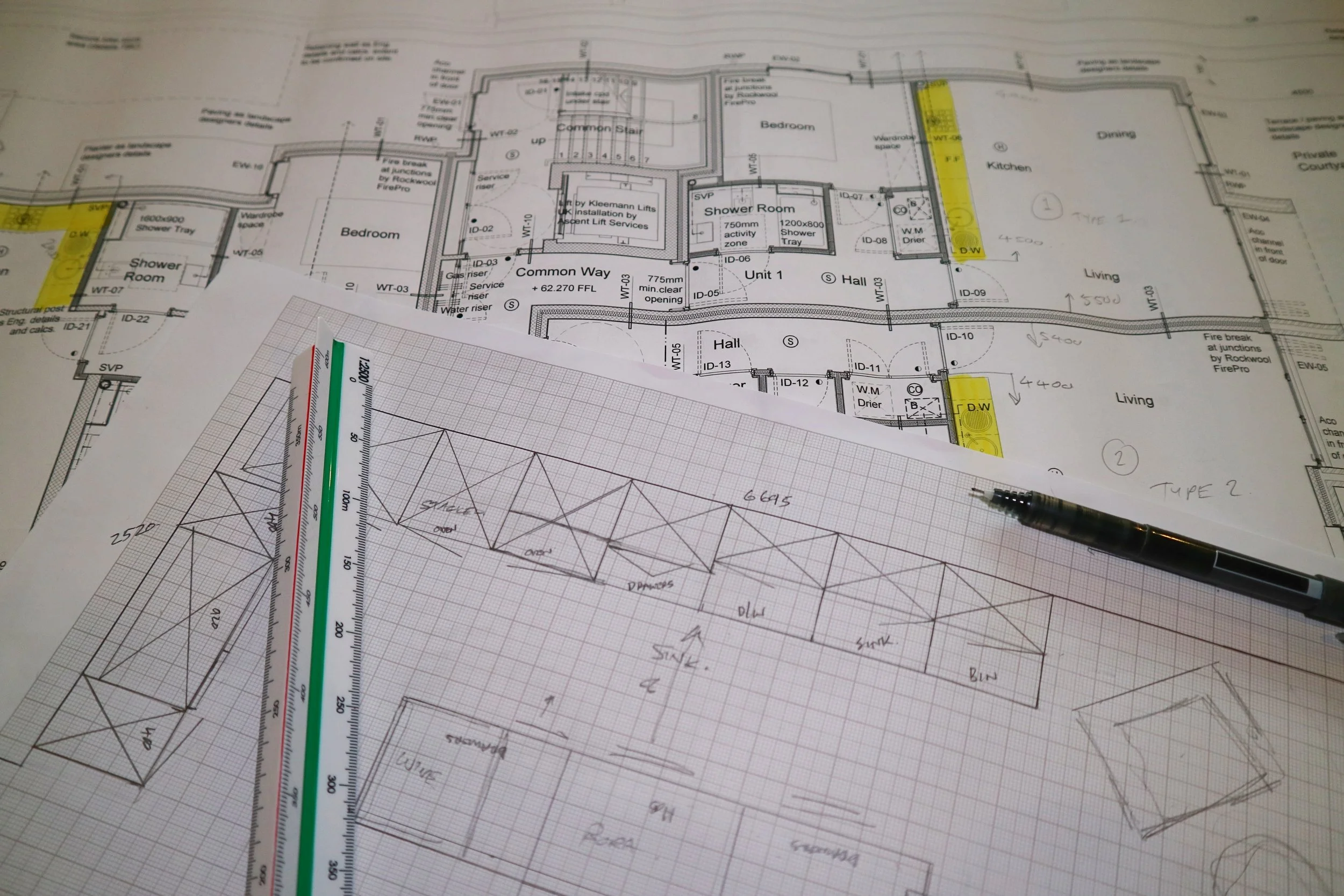 Kitchen Architectural blueprints and construction plans laid out on a desk, with a scale ruler and pen.