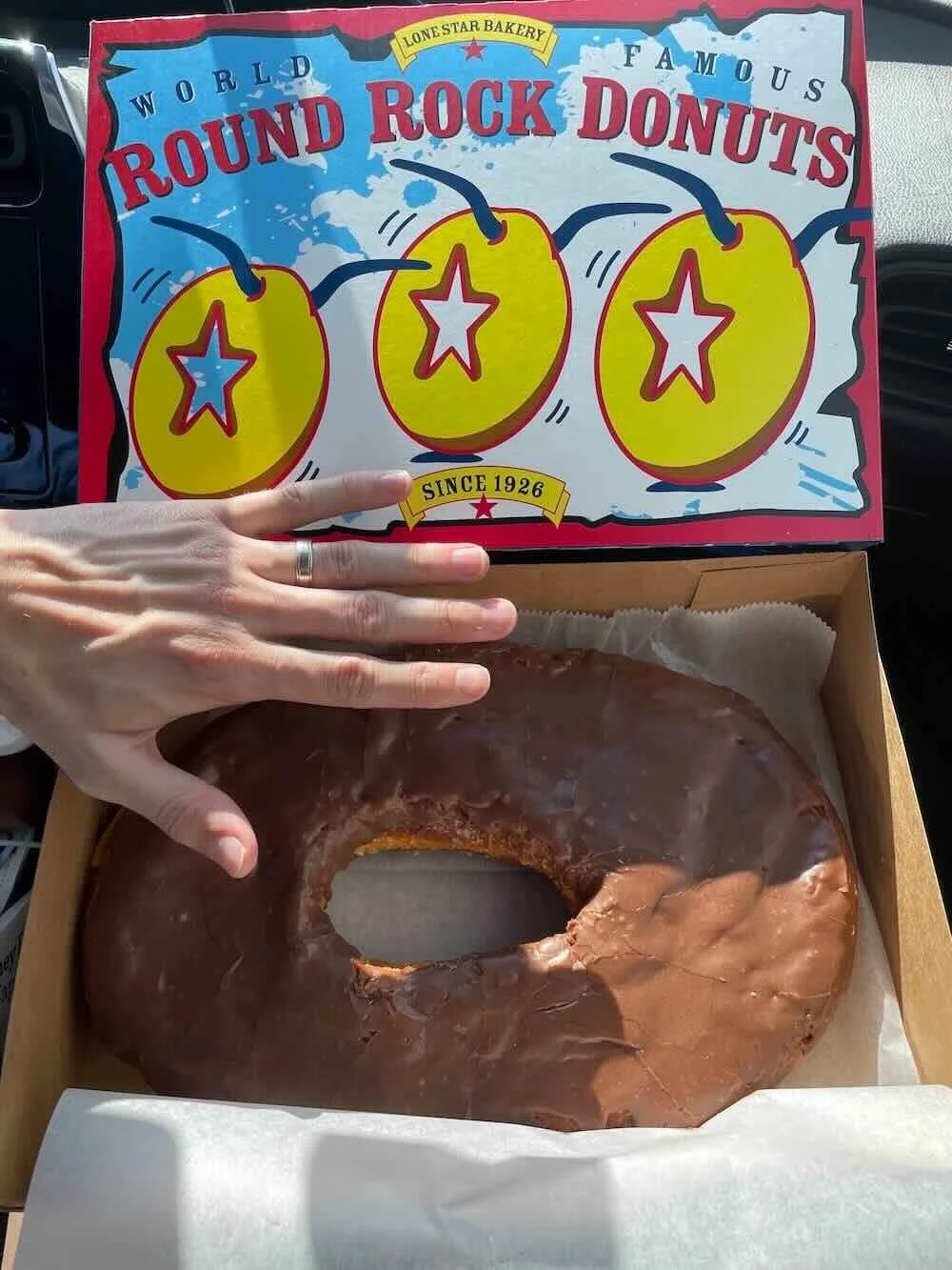 man's hand over large chocolate donut to highlight donut size