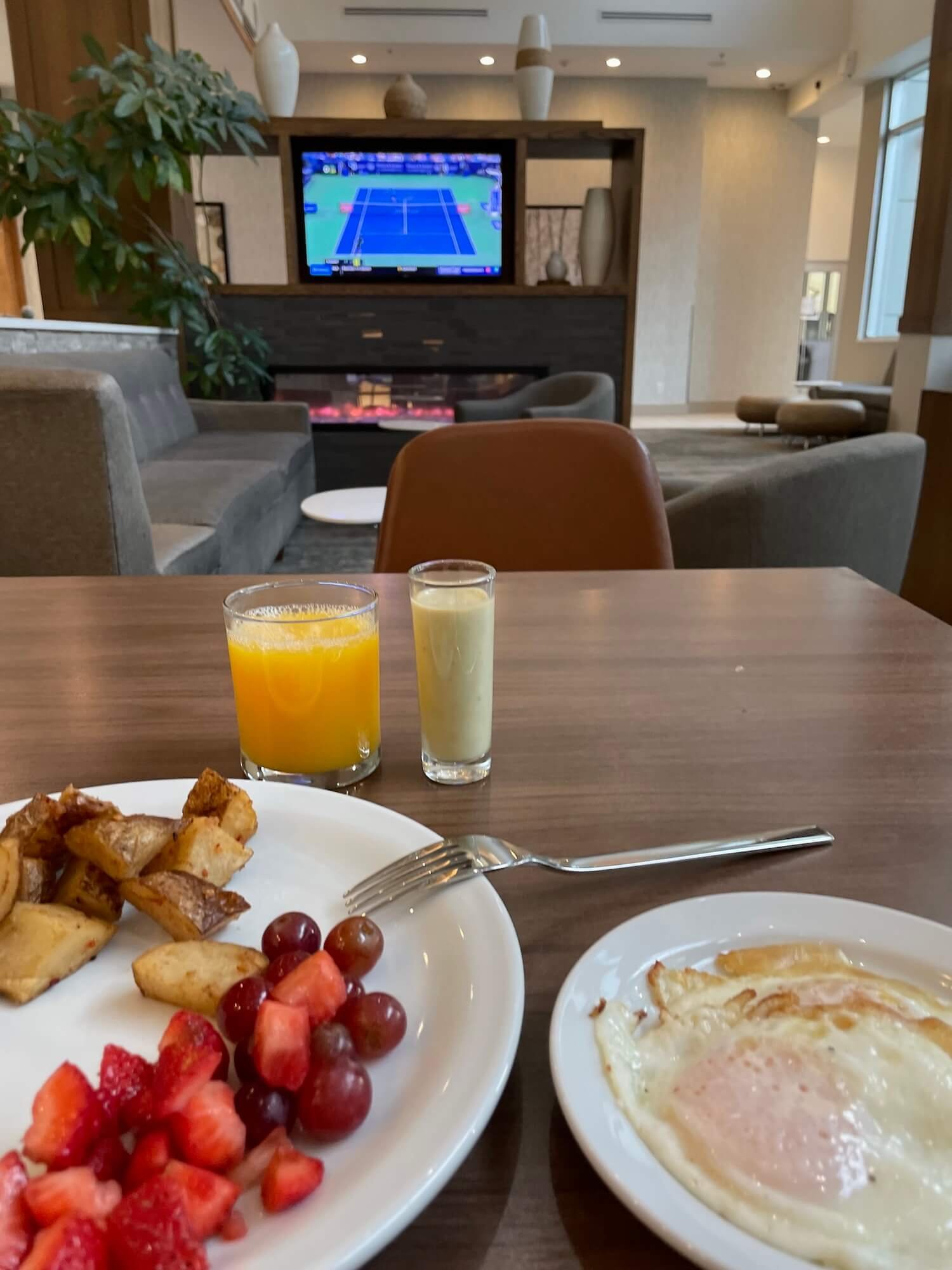 breakfast including fresh fruit, fried egg, potatoes, orange juice, and smoothie