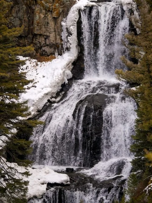 partially frozen waterfall lined with snow