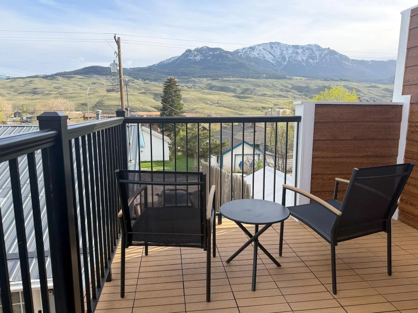 Balcony with two black chairs, small round table, and mountain landscape with snow-capped peaks in the background.