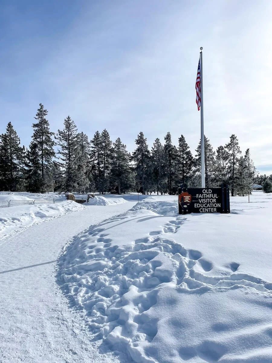 welcome sign for Old Faithful Visitor Center next to snowy walkway