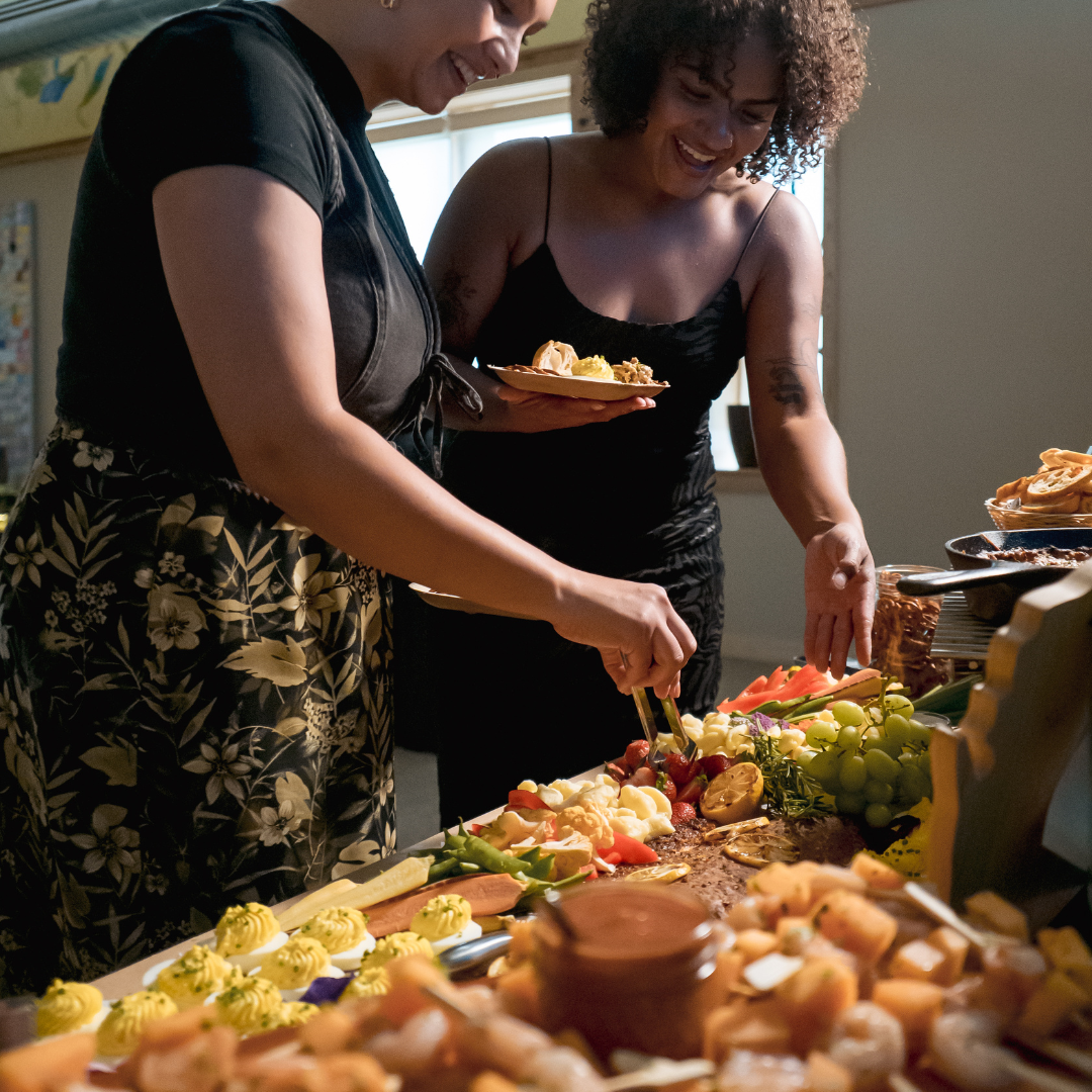 Holiday buffet with seasonal dishes and two women selecting appetizers to put on their plates.