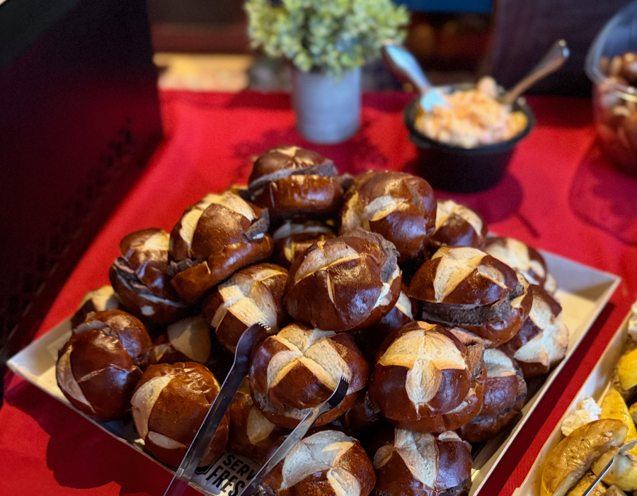 A tray of soft pretzels with a golden-brown crust and a cross-cut scoring pattern on top, displayed on a table with a red tablecloth.