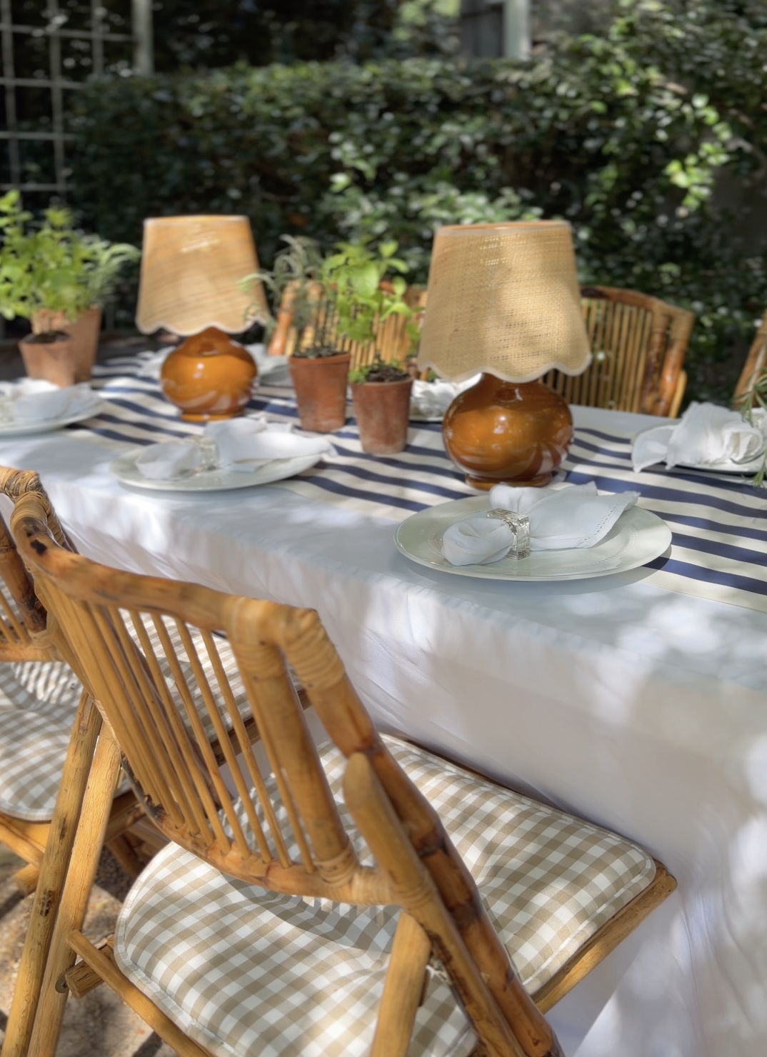 Outdoor dining table set with cordless table lamps, gingham chair cushions and a striped cloth