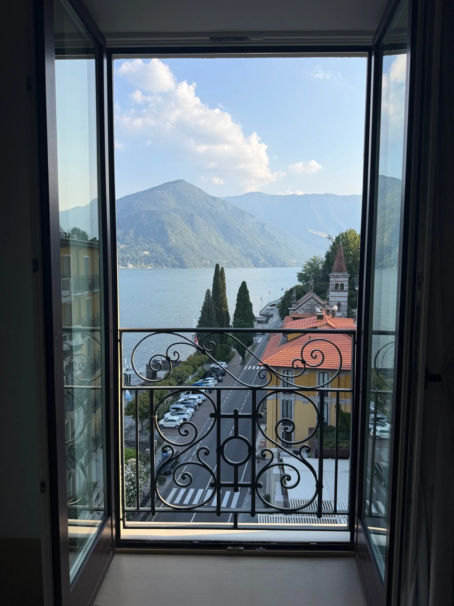 Open balcony doors with a wrought iron railing looking out over a Lake Como village