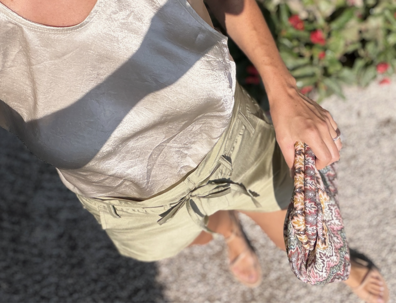 Cream top, olive linen shorts and a floral block print clutch on a gravel path