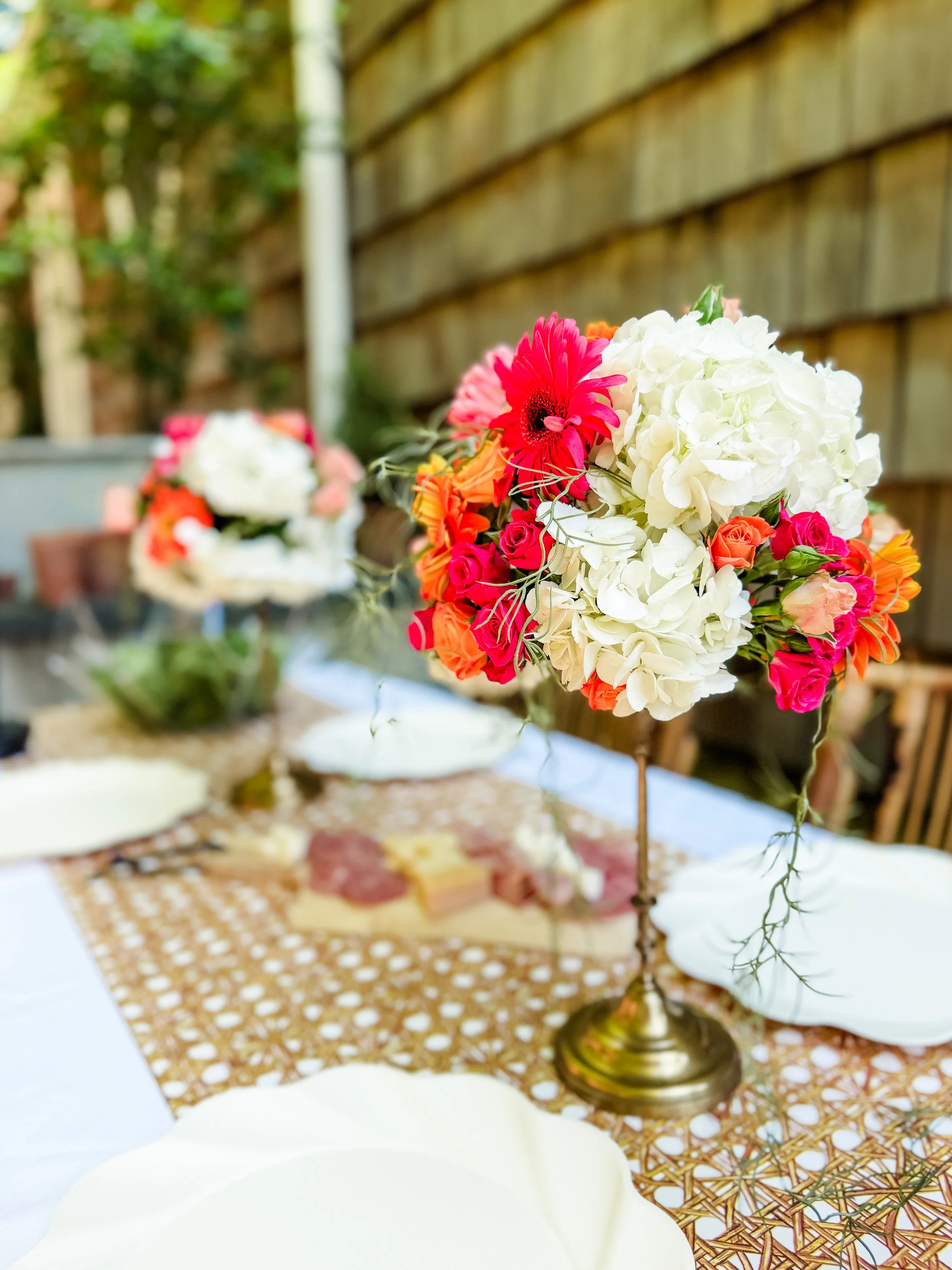 Outdoor tablescape with a tall pink and white floral centerpiece on a woven lace runner