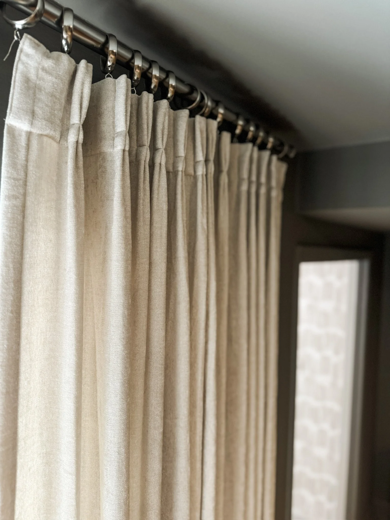 Natural linen pinch-pleat curtains hanging from a metal rod