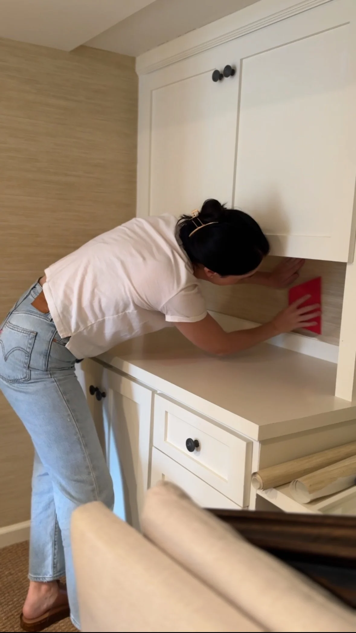 Smoothing peel-and-stick wallpaper into place on the wall above a white dresser