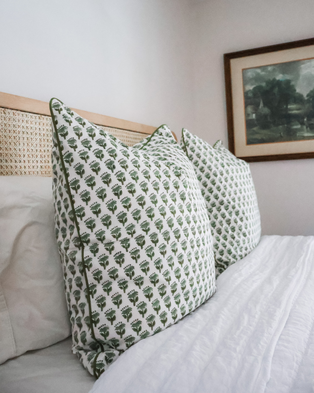Green block print pillow on white bedding against a cane headboard