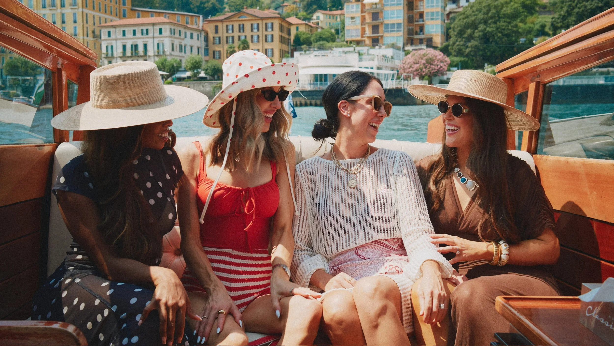Four friends in swimsuits and straw sun hats on a wooden boat in Italy