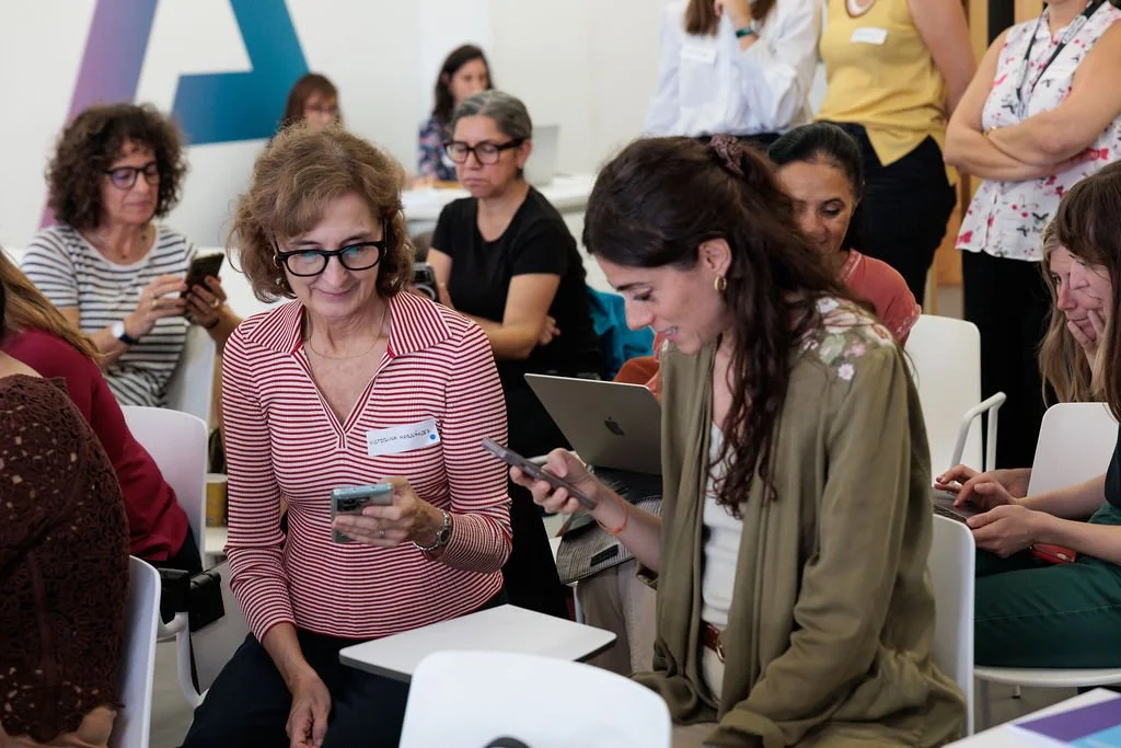 Participantes sentadas consultan teléfonos y un ordenador durante una dinámica