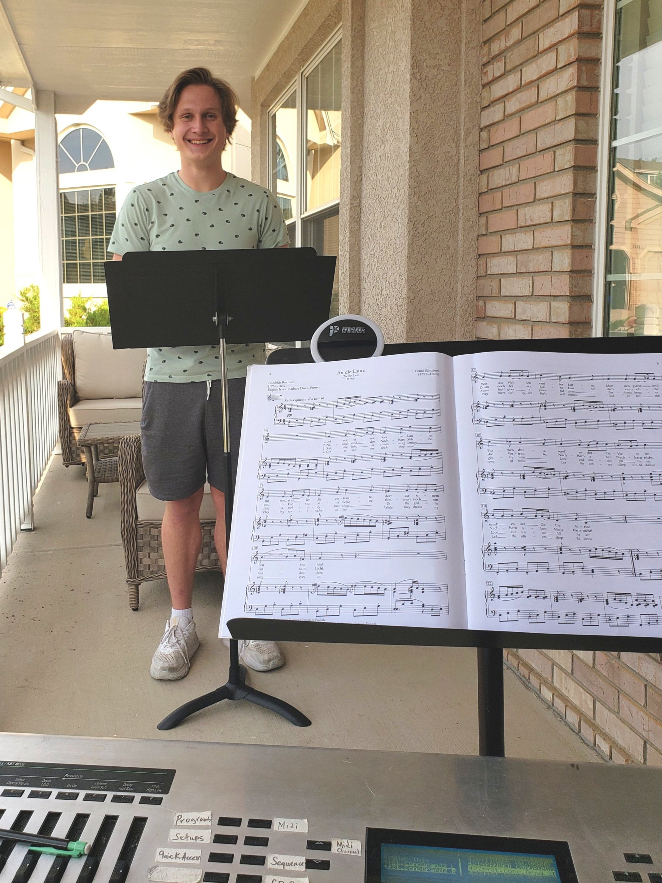 Teen boy at music stand in outdoor voice lesson with piano.