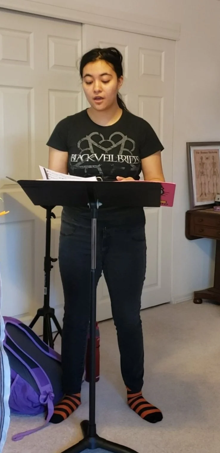 Teen singer singing in front of music stand with sheet music.