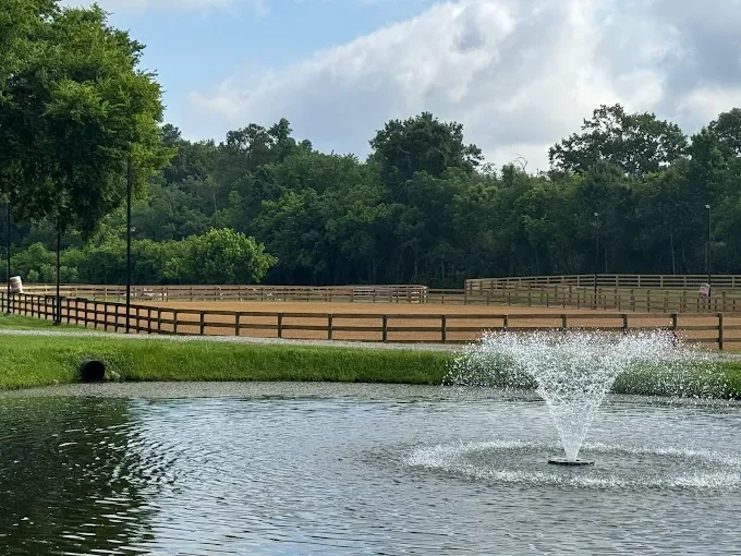 Lush greenery with a small pond, fountain, and fenced rings for horses to ride in.