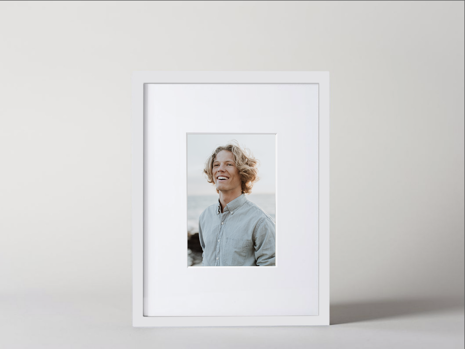 Framed photo of a smiling person with wavy hair wearing a button-up shirt, standing outdoors near the ocean.