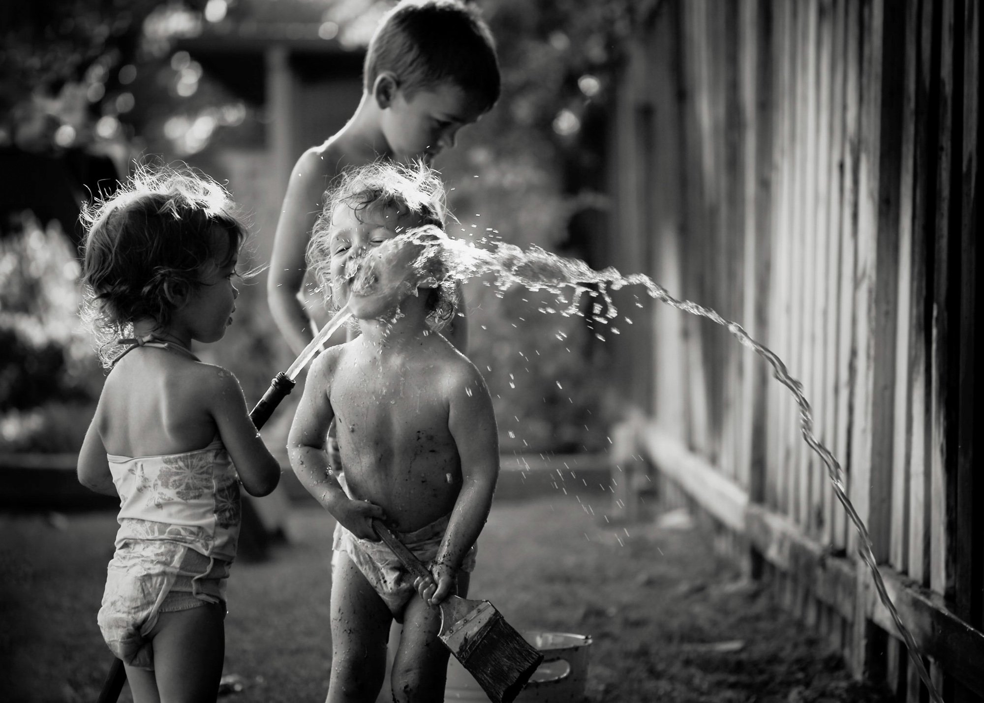 Orange County Child and Family Photography. Three young children playing with a water hose in a backyard, black and white photo.
