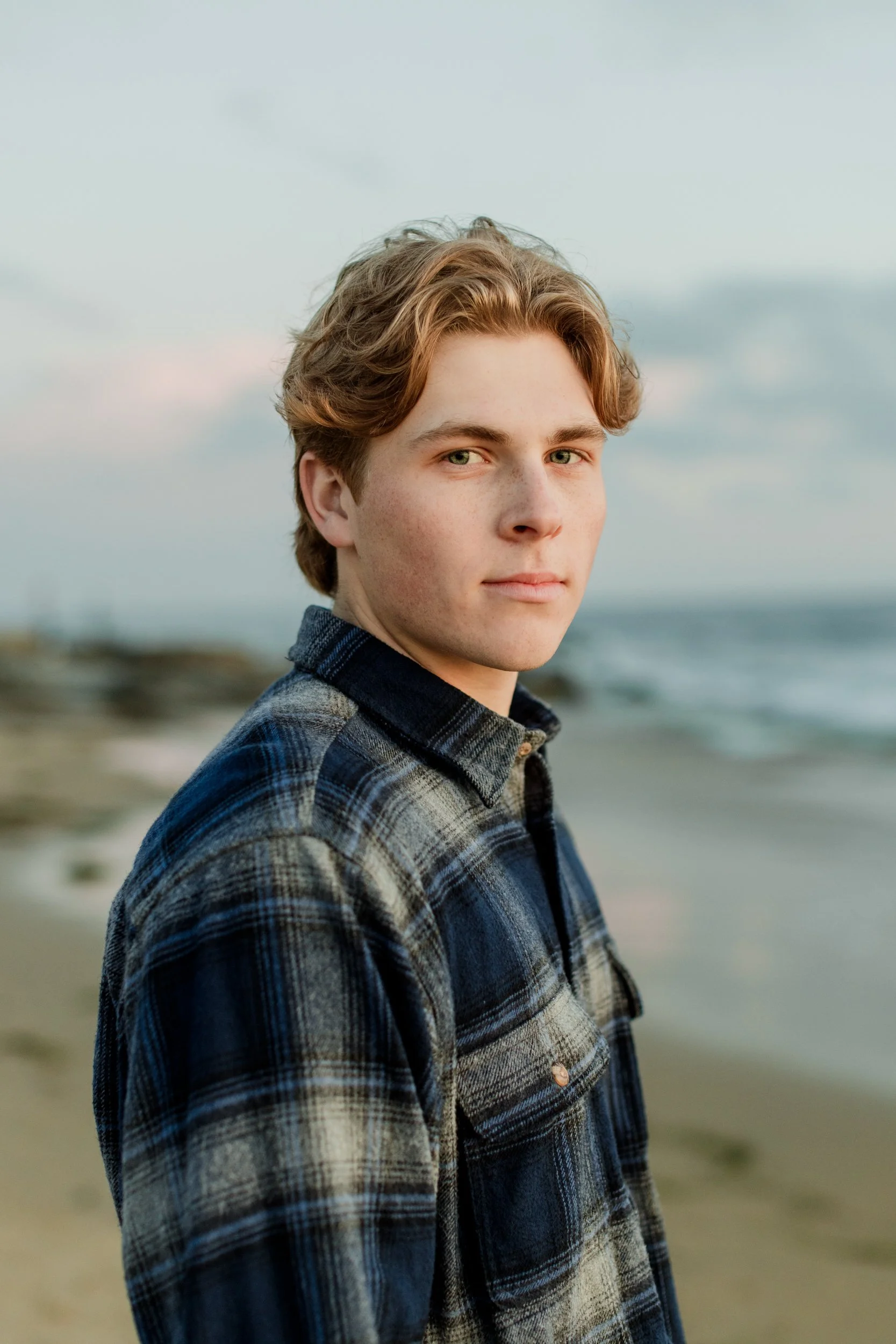 Young man in a plaid shirt standing on a beach.