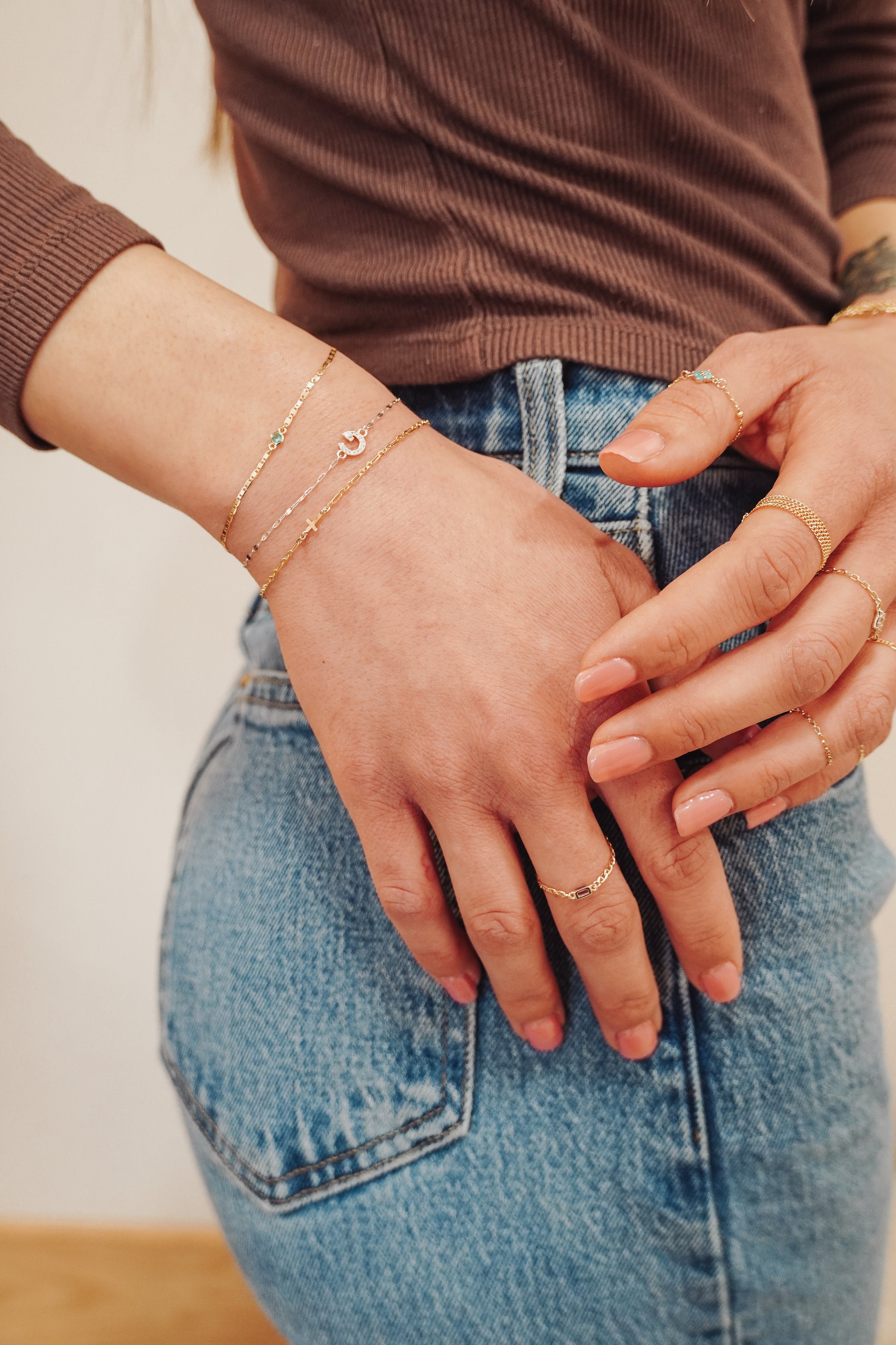 A person wearing multiple solid 14k permanent gold bracelets, rings, and a delicate necklace from Lucky Gold in Sacramento