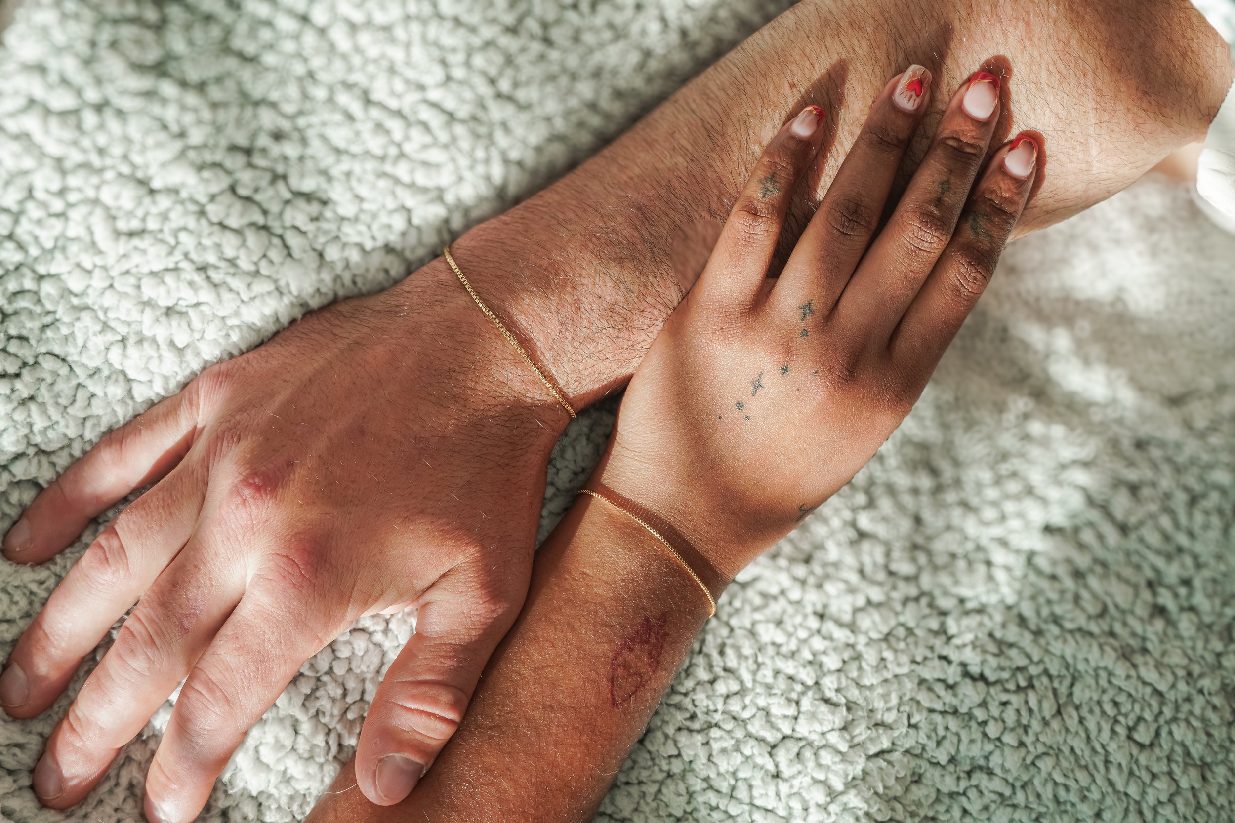 Two hands wearing permanent solid 14k gold bracelets