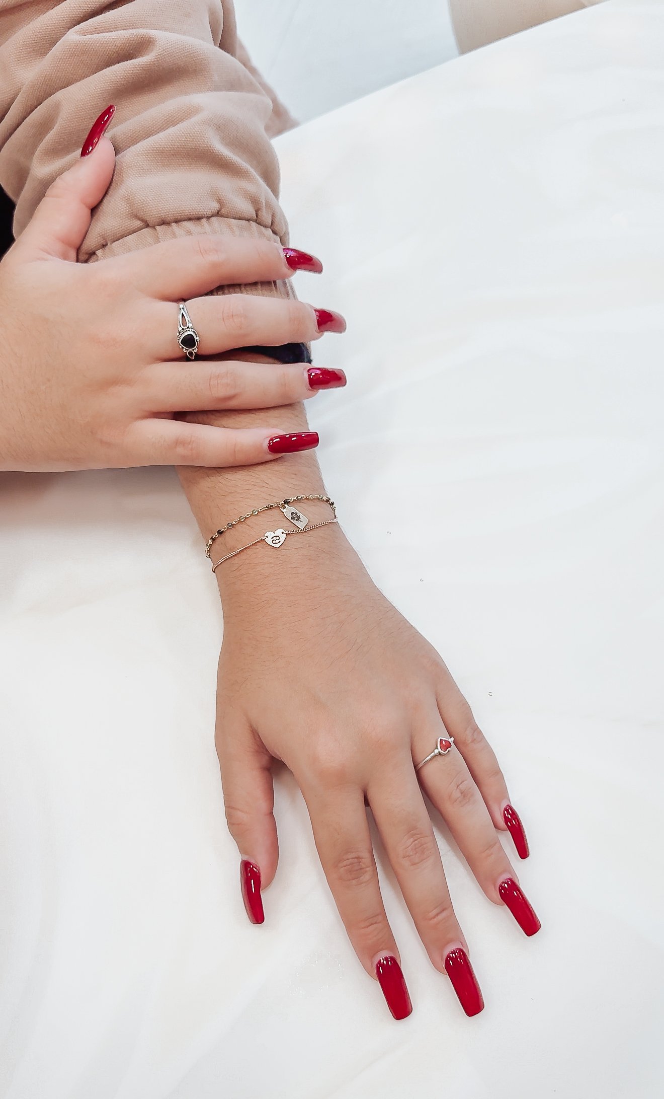 Two hands with red manicured nails and silver permanent jewelry, bracelet, and ring in Sacramento.