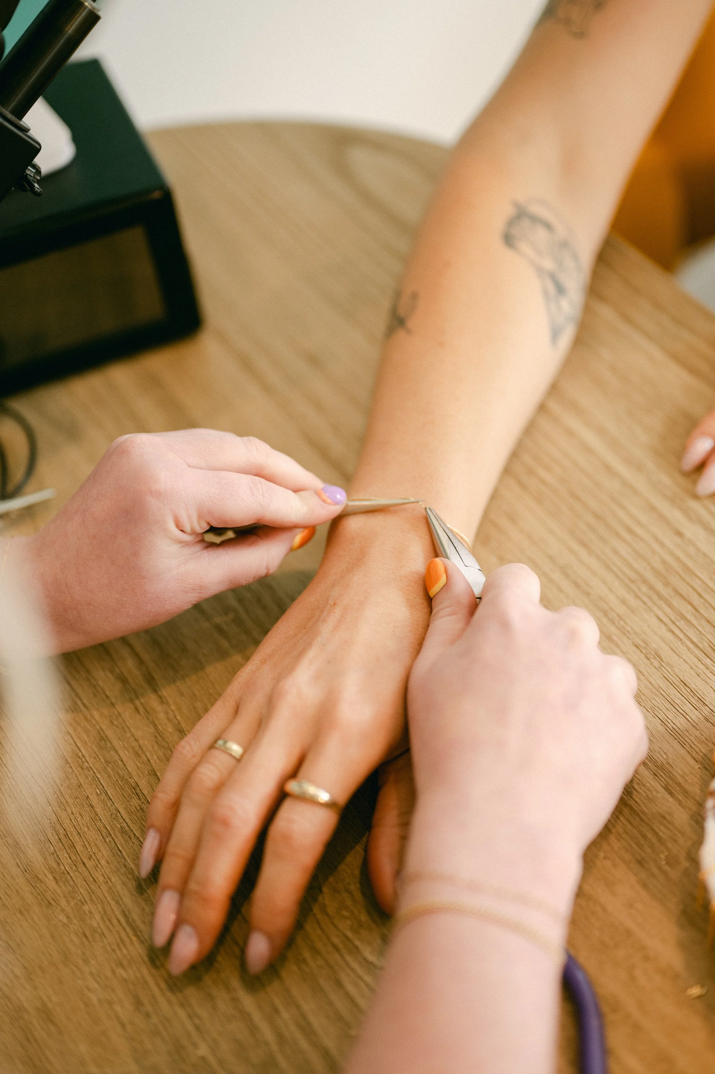 A person receiving a tattoo on their wrist at a tattoo parlor, with a person holding the tattooing tool.