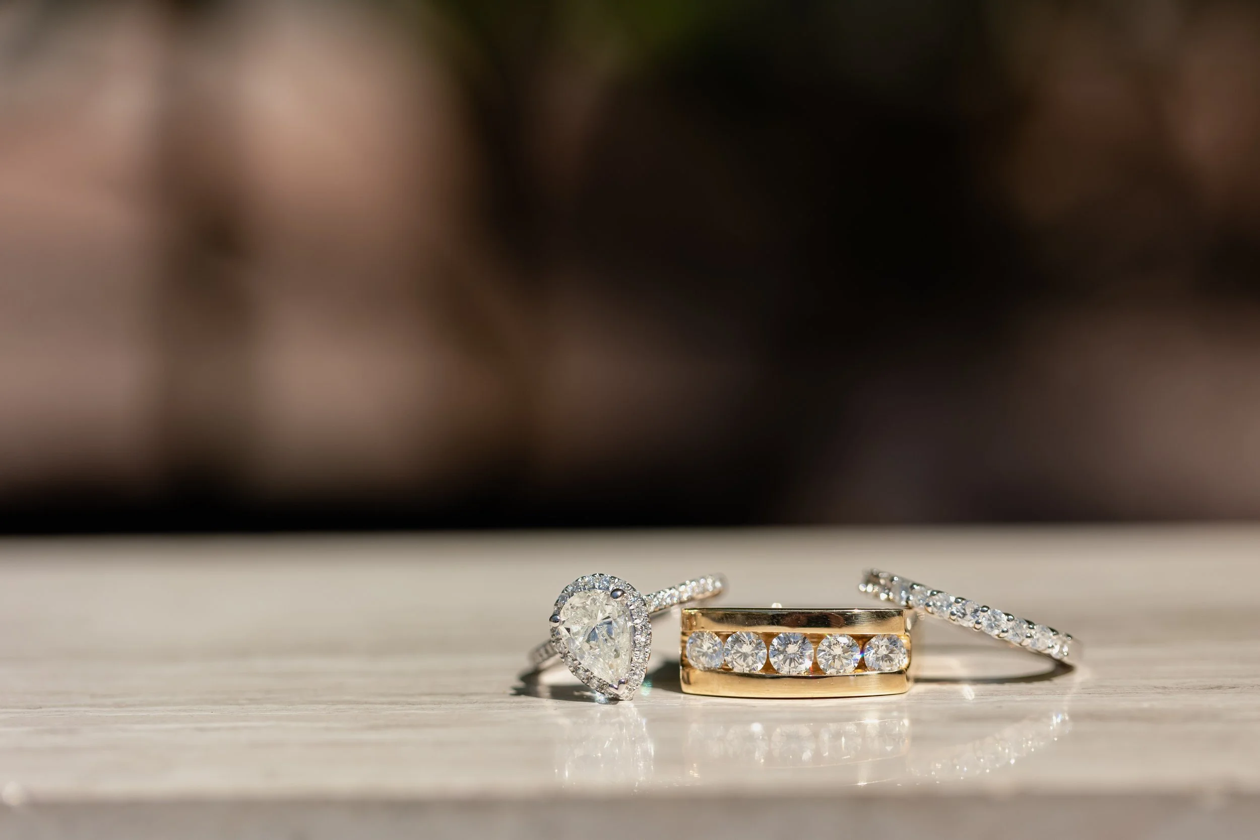 Three rings with diamonds on a light-colored wooden surface, with a blurred background.