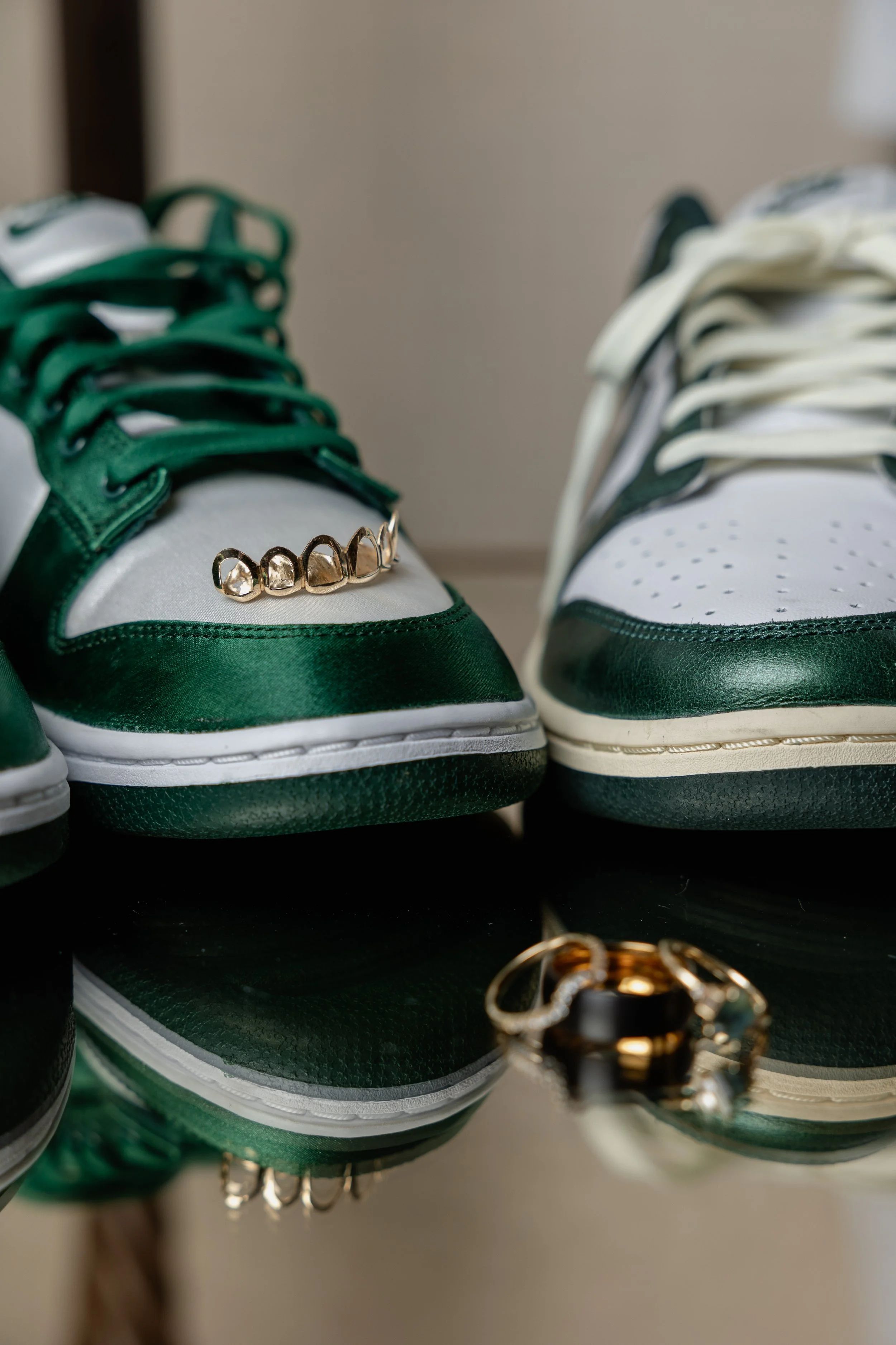 Pair of green and white sneakers with rings placed on top, and a ring is also visible on the reflective surface in front of the shoes.