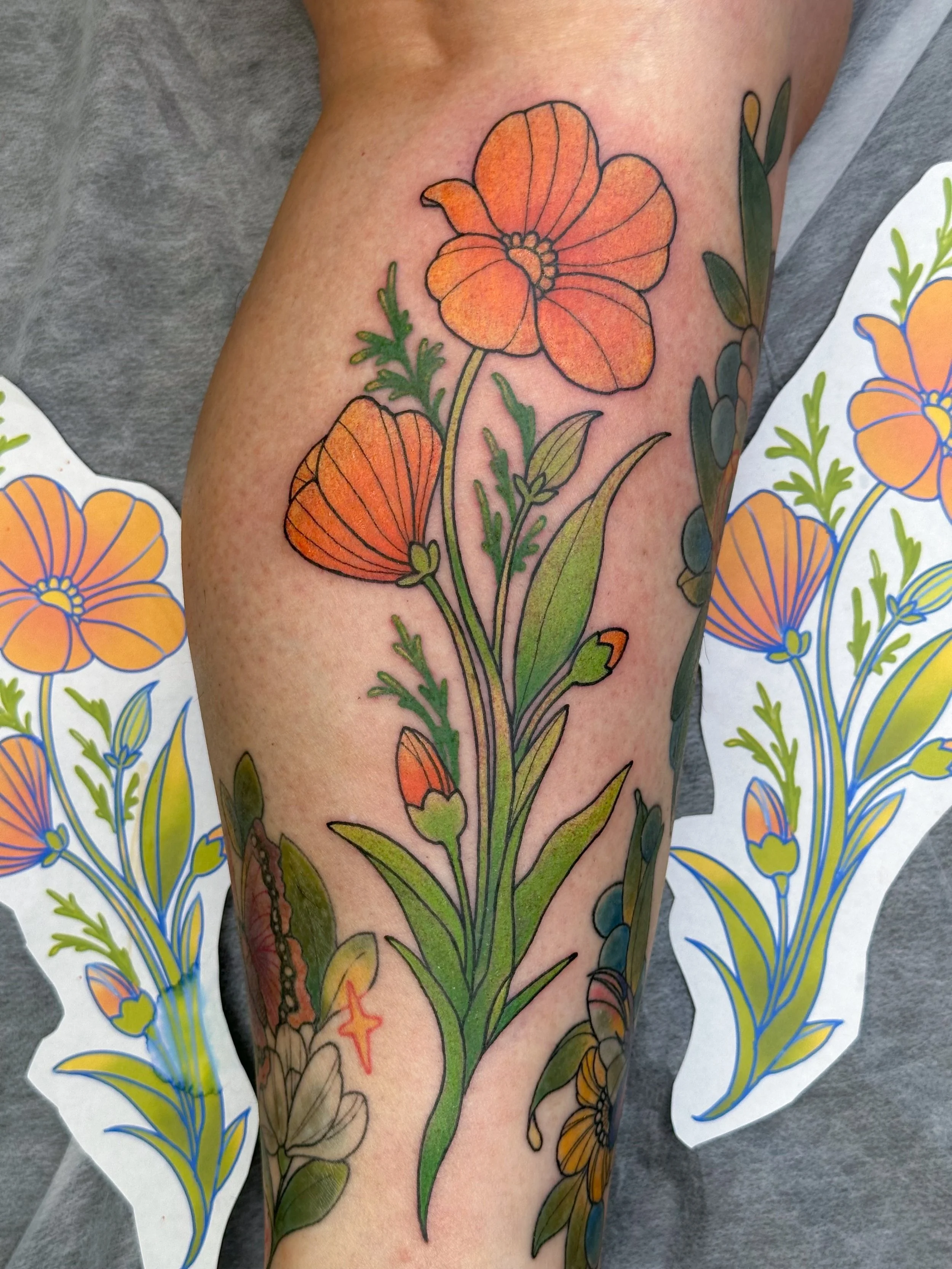 Colorful floral tattoo featuring orange poppies and green leaves on a person's arm, with tattoo stencil paper nearby.