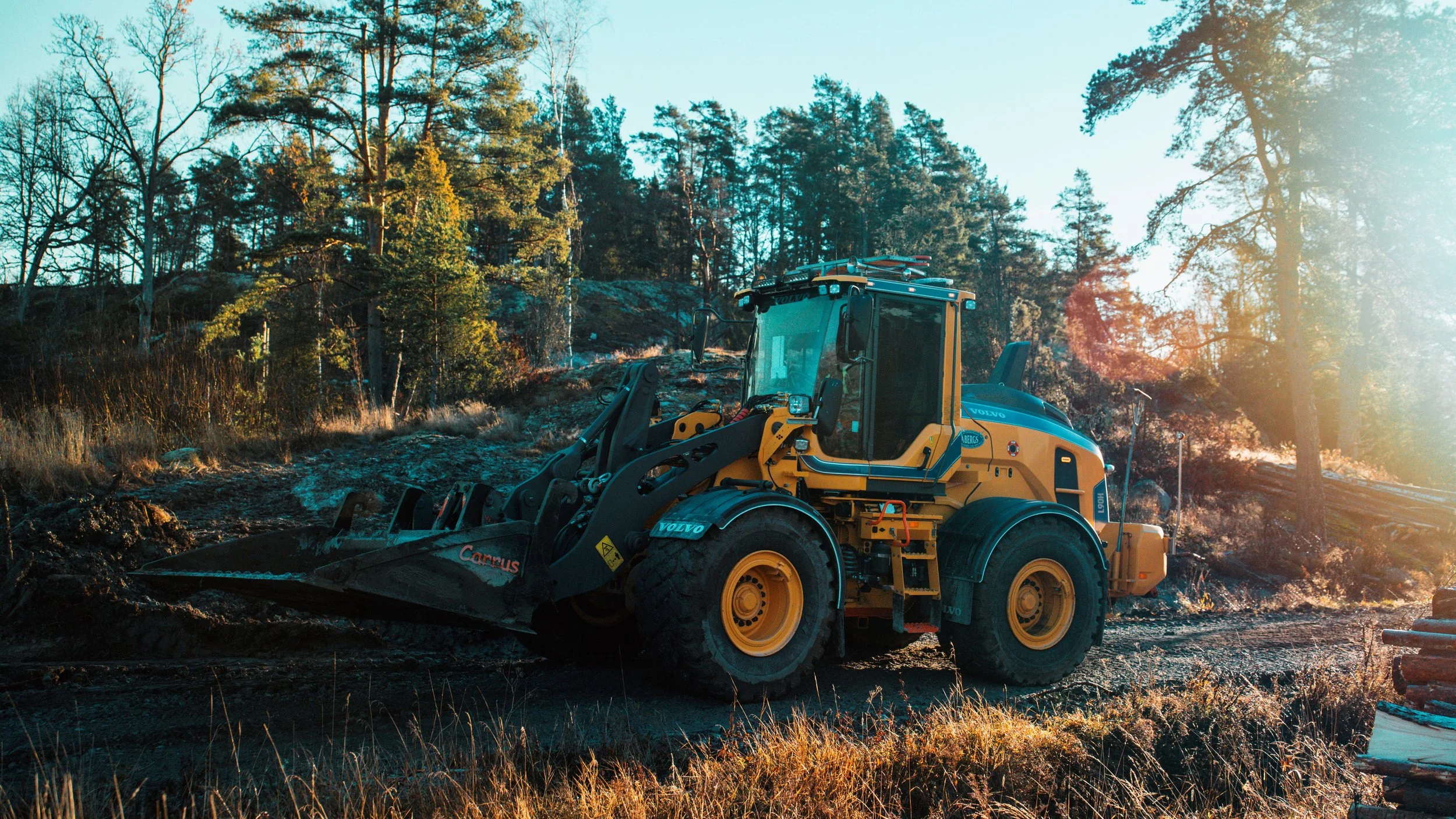 En gul grävmaskin på en byggarbetsplats i skogen under tydlig dagbelysning.