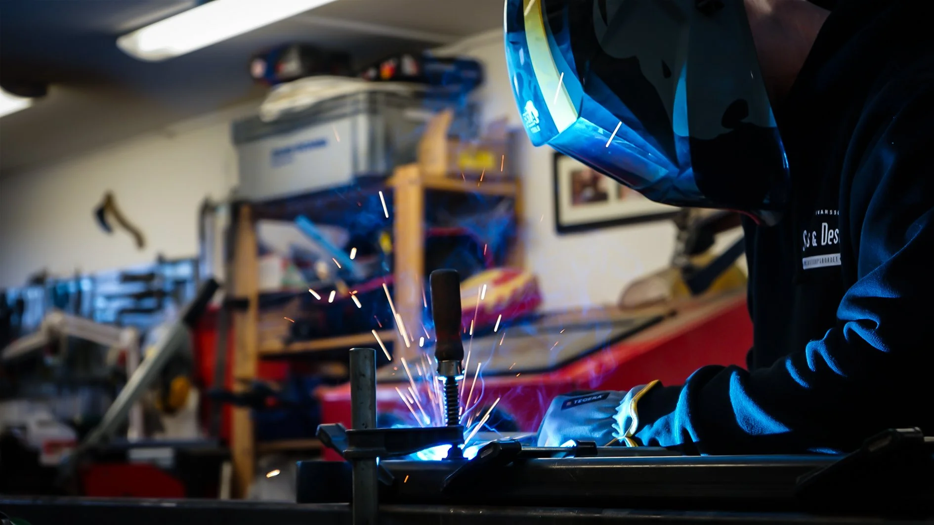 Person som svetsar i ett verkstad eller garage, med skyddshjälm och handskar.